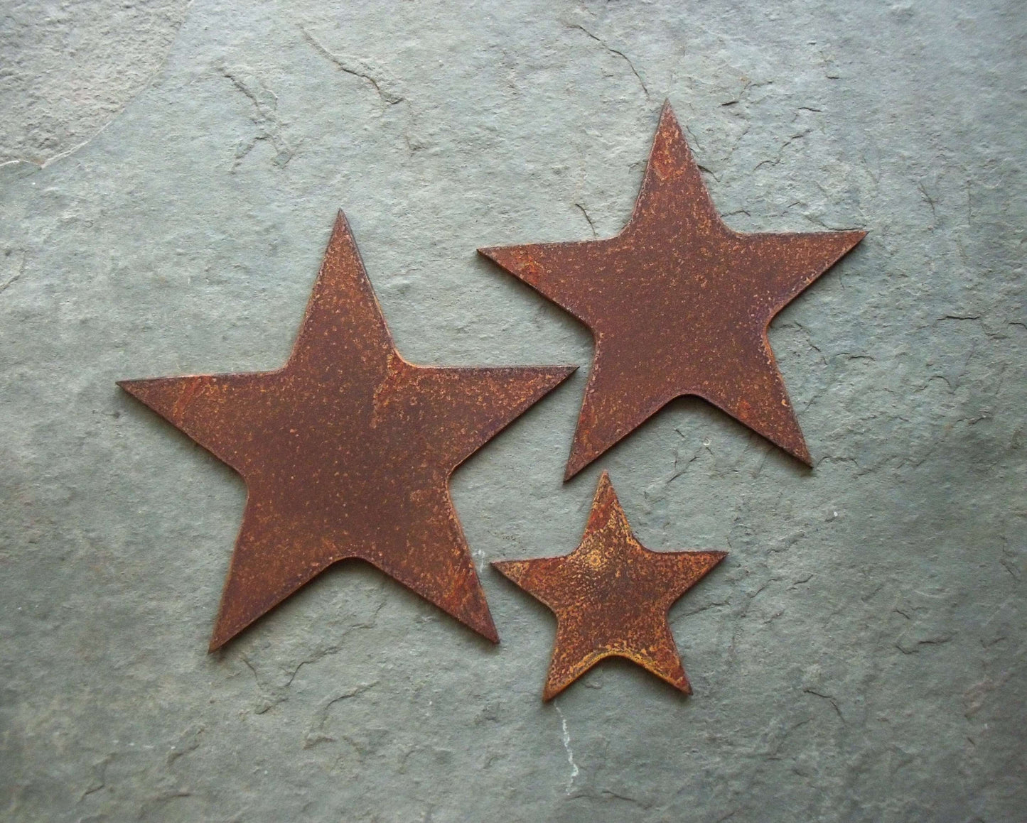 Rusty metal lucky stars set of three garden decorations on a grey stone background, unique rusted patina effect.