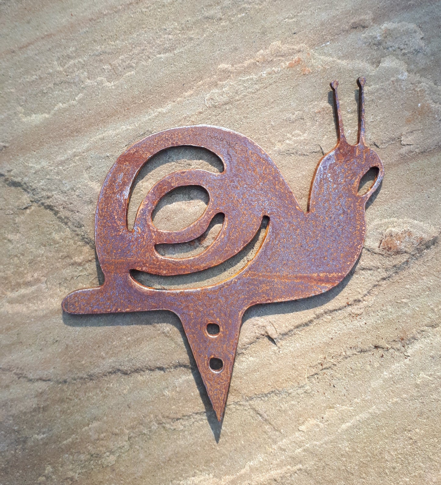 Rusty metal snail garden decoration with pot spike option shown on a stone background.