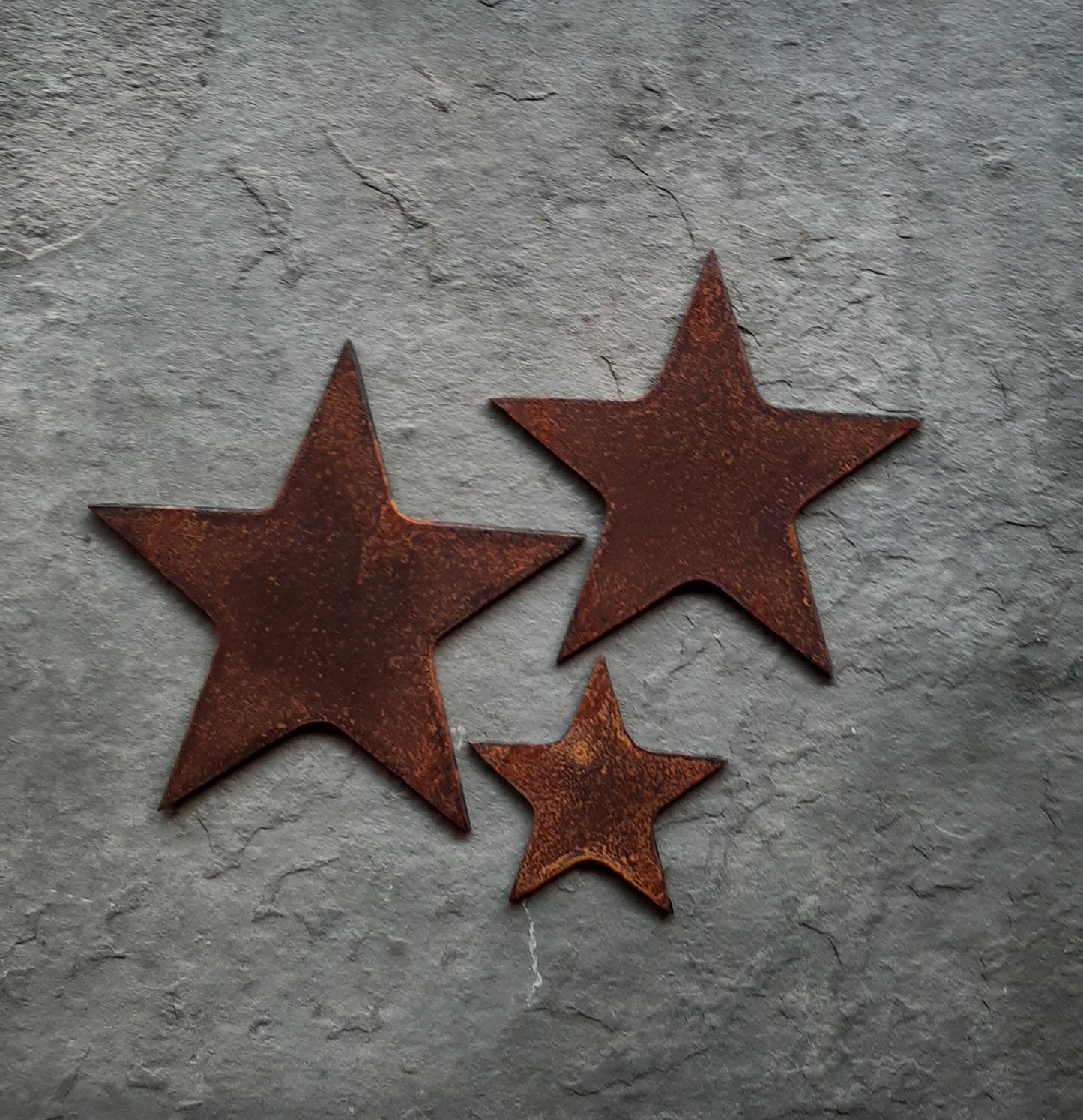Rusty metal stars set on a grey stone slab, features 3 different sized stars, unique rusted steel designs.