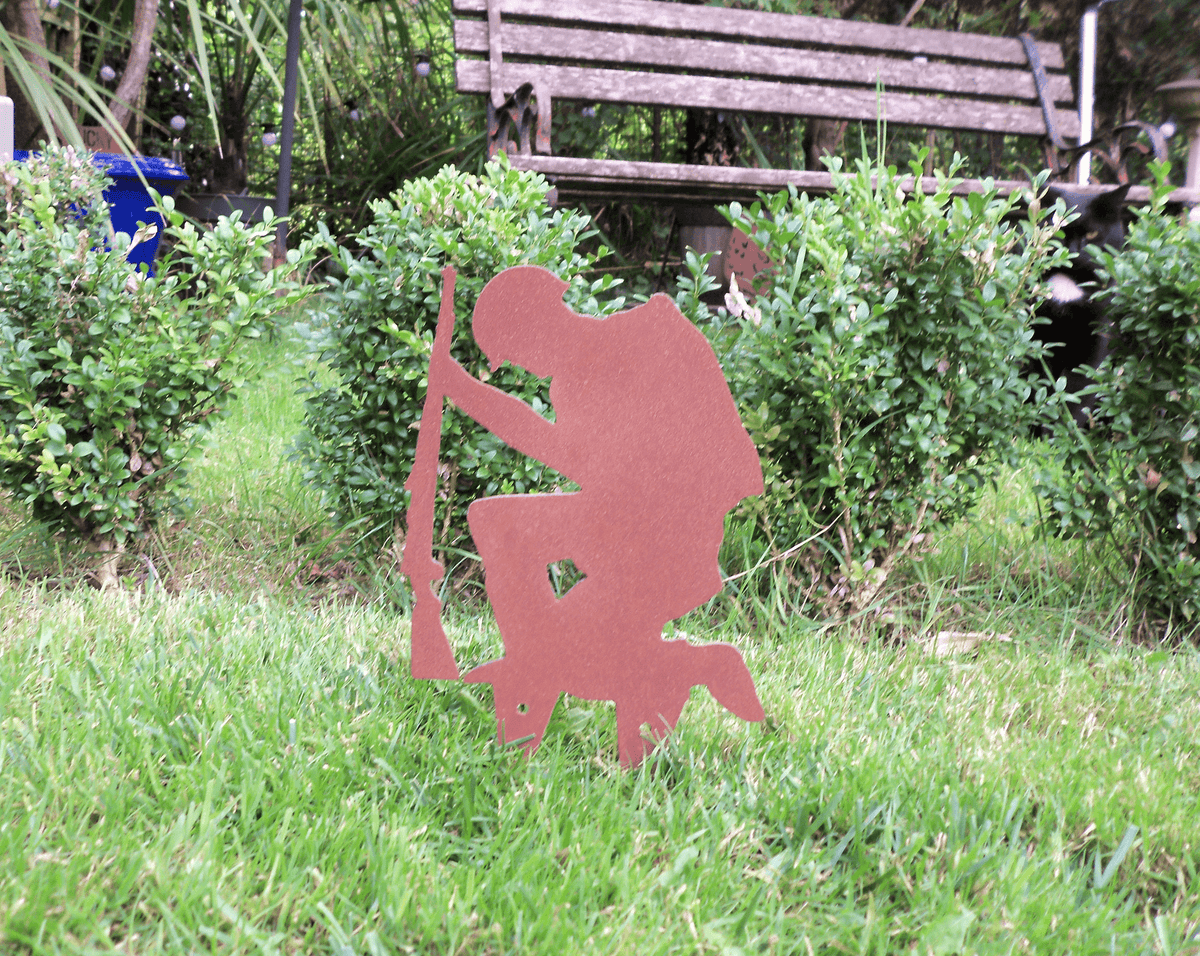 Rustic Steel SOLDIER Garden Ornament in a garden, featuring a kneeling soldier holding a rifle with a rusted finish.