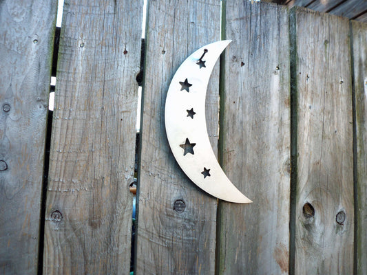 Metal crescent moon garden ornament with star cutouts attached to wooden fence.