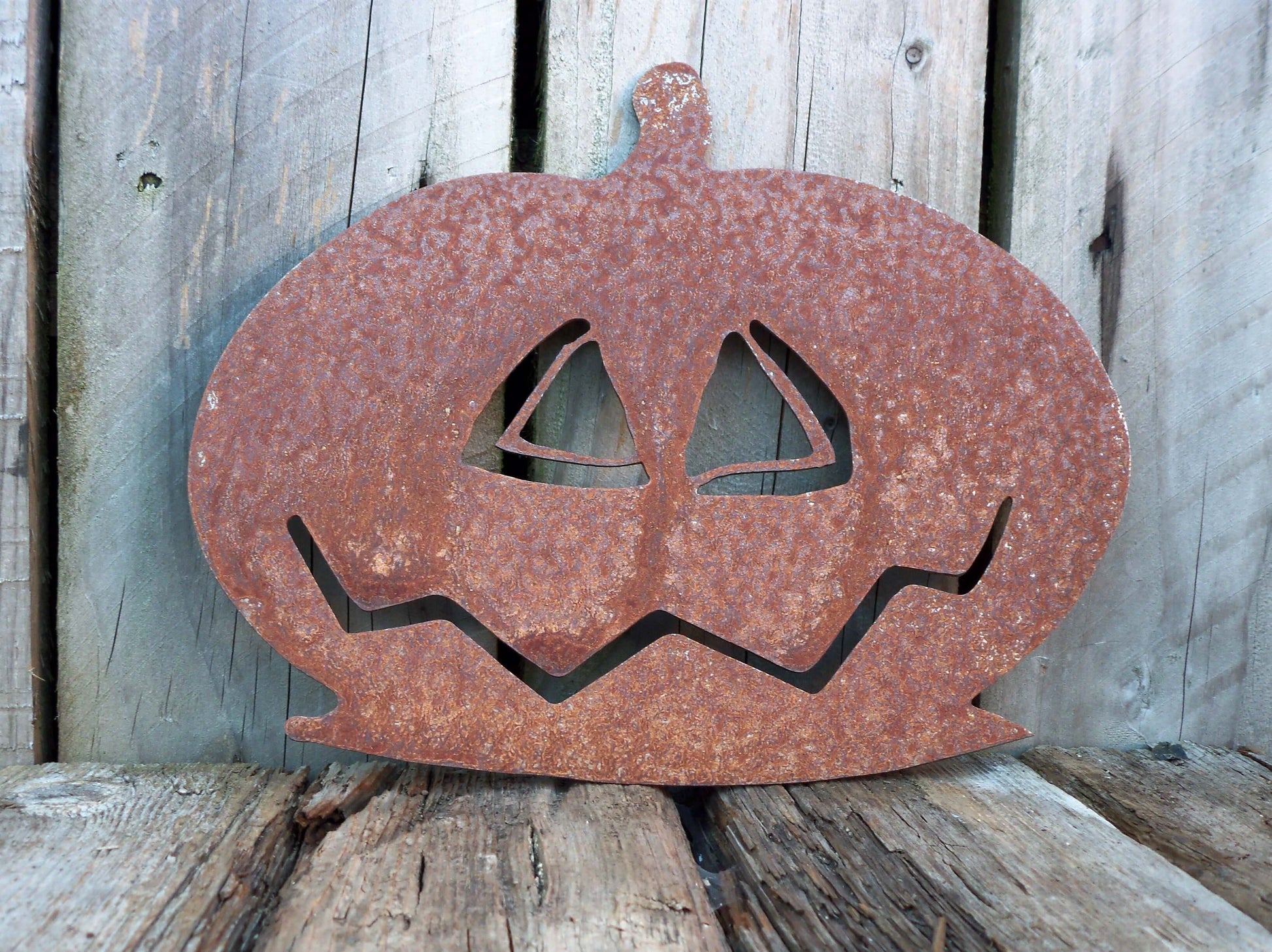 Rustic rusted metal pumpkin garden ornament with carved face, perfect for Halloween decor and outdoor artistic display.