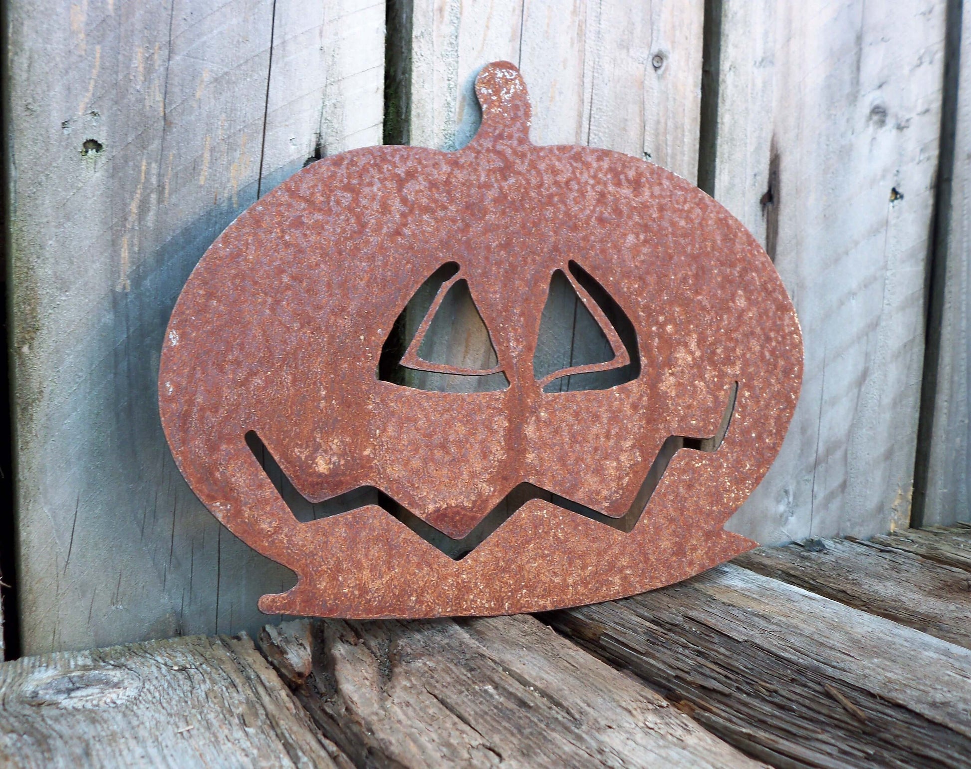 Rusty metal pumpkin garden ornament against wooden background, rustic Halloween decor, unique patina effect.