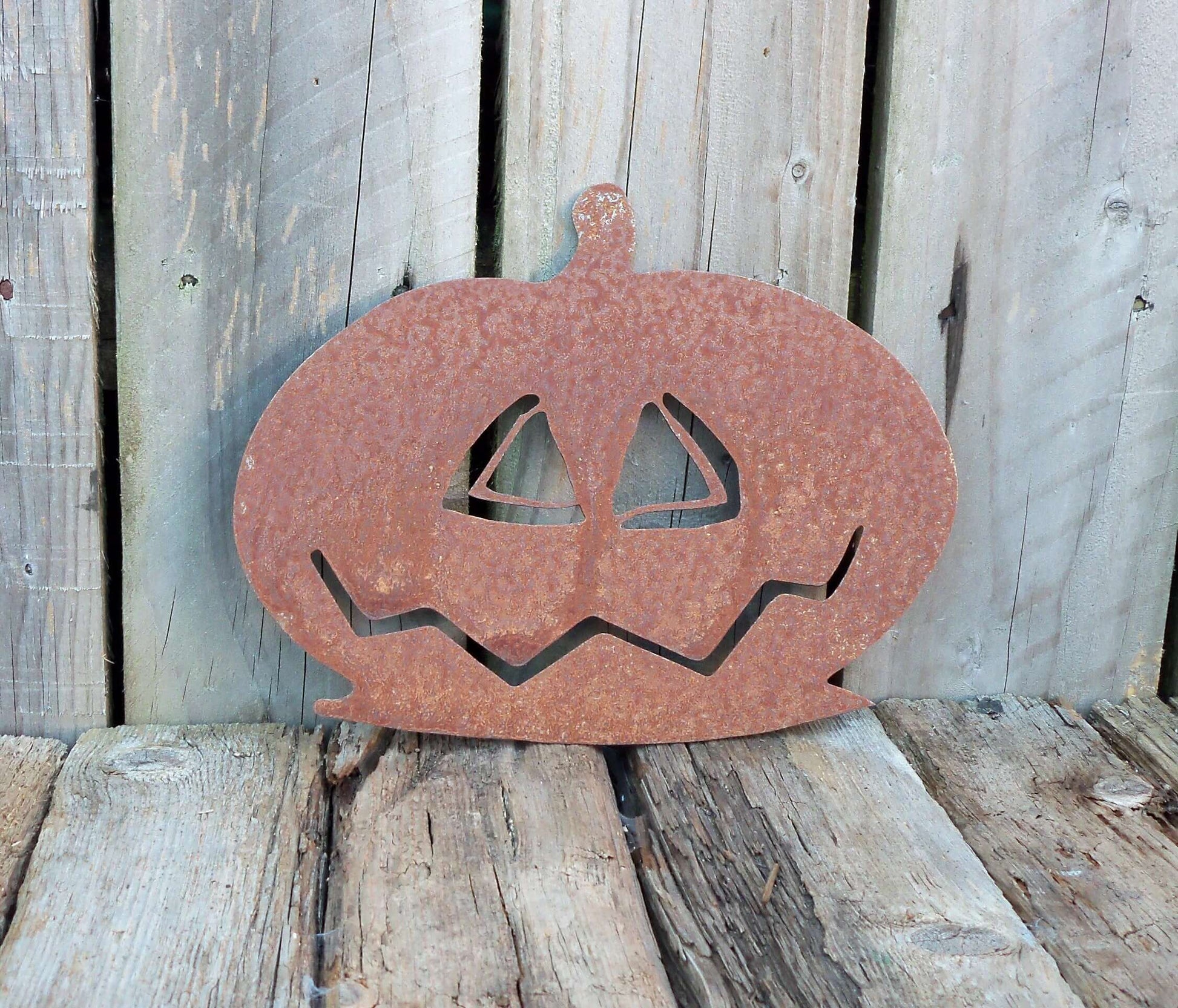 Rustic metal pumpkin garden ornament on wooden deck, scary Halloween decor