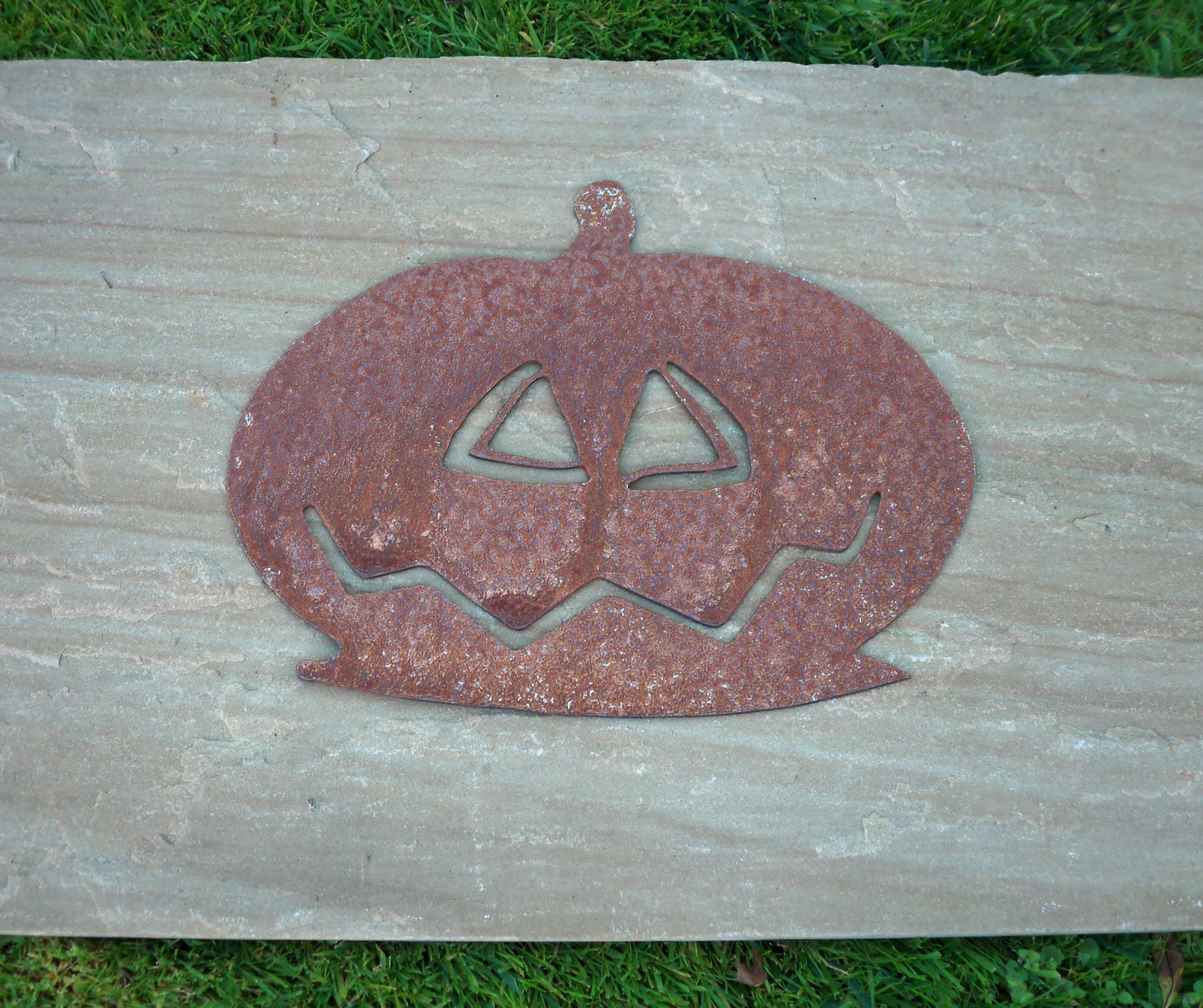 Rustic garden decor; rusty metal pumpkin ornament on stone slab, unique rusted patina, industrial-style garden art.