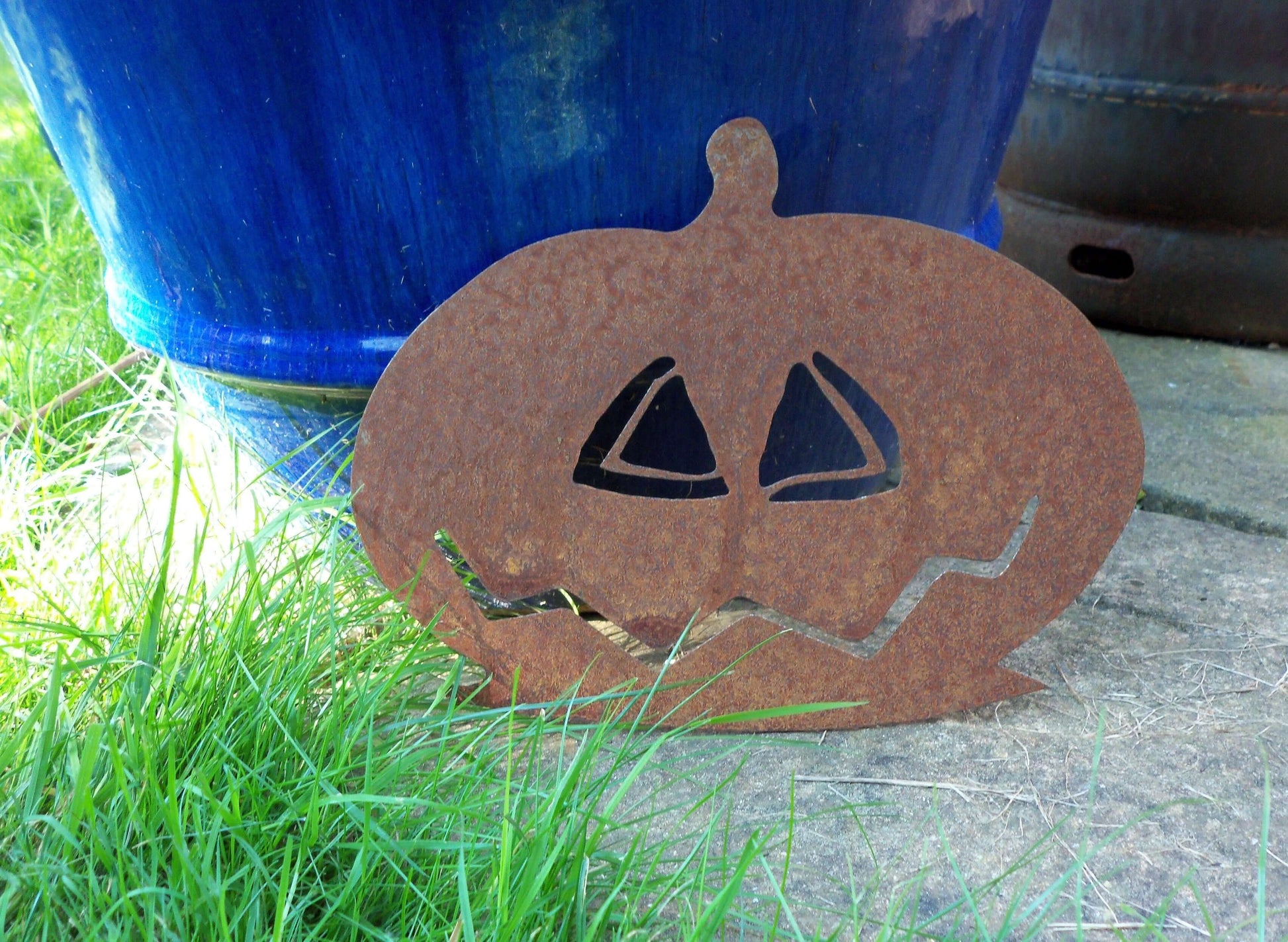 Rustic metal pumpkin garden ornament in front of blue pot, ideal Halloween decor.