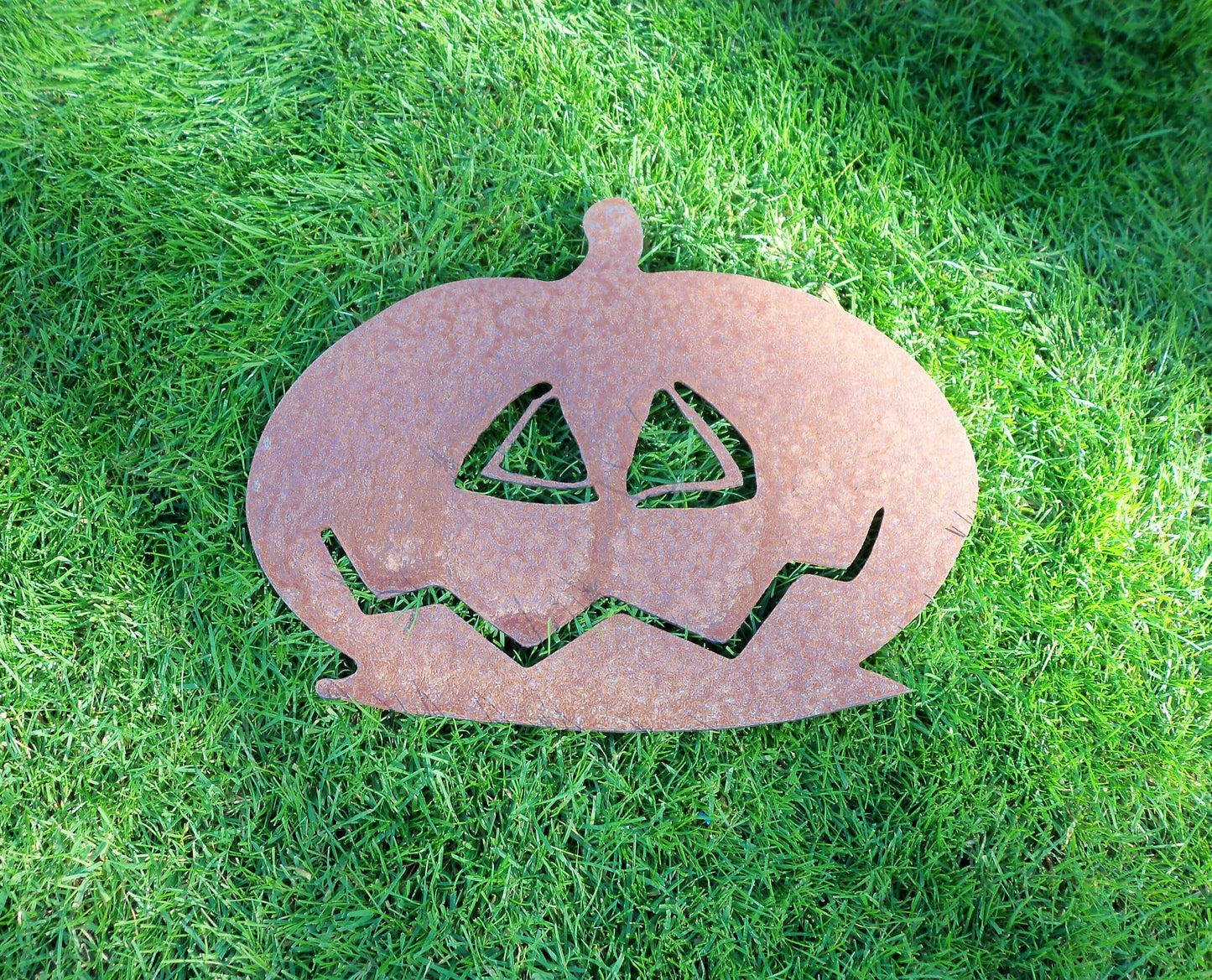 Rustic rusty metal pumpkin garden ornament on green grass, ideal for Halloween decor and garden decoration.