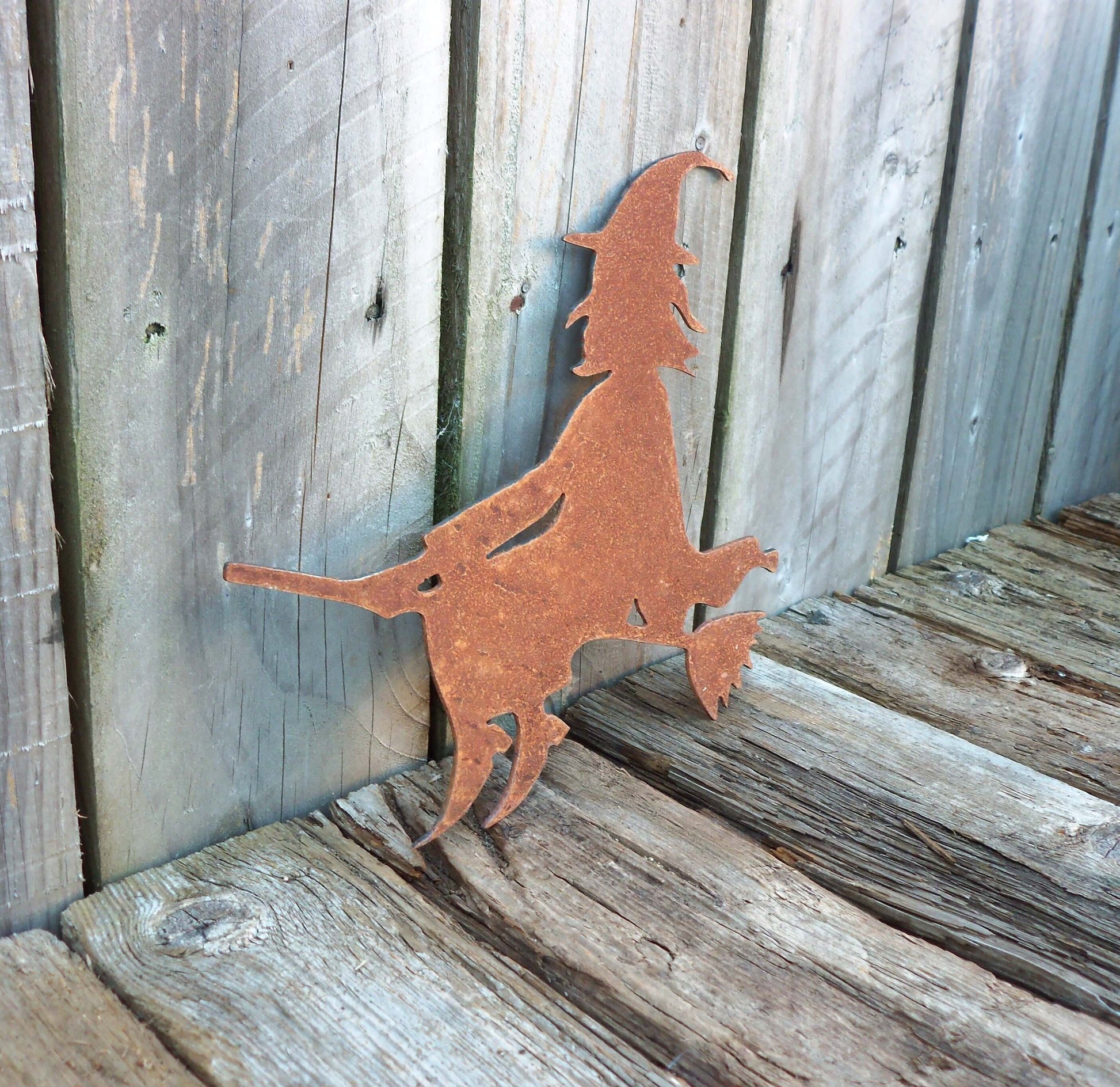 Rustic metal witch garden ornament on wooden deck, Halloween decor