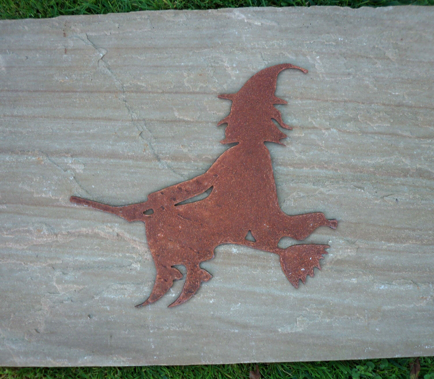 Rustic rusty metal witch on broomstick garden ornament, Halloween decor, shown on stone background.