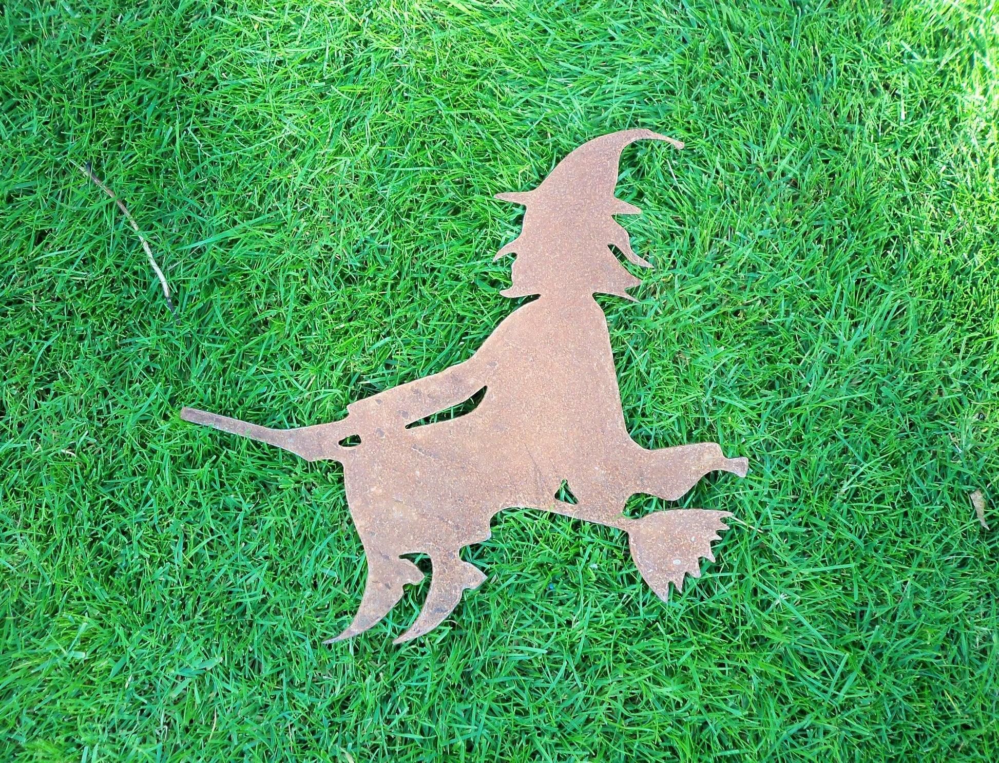 Rusty metal witch on broomstick garden ornament on grass, rustic Halloween decor, 2mm thick steel, unique rusted patina effect.