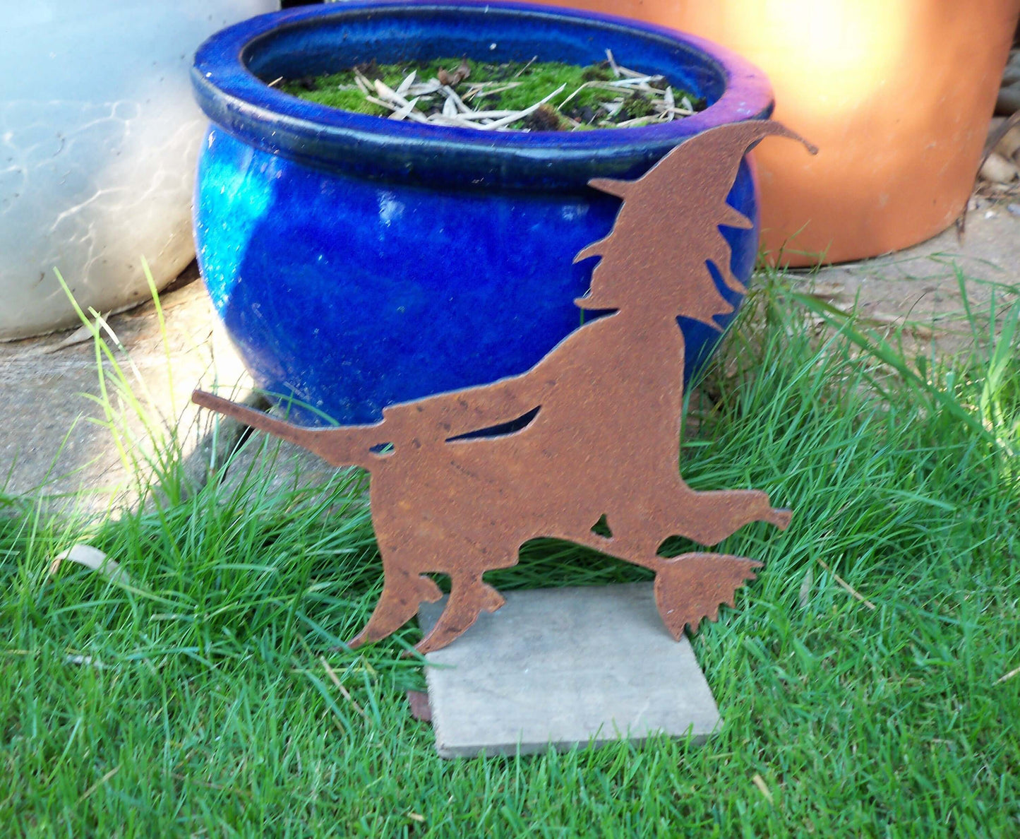 Rustic metal witch on broomstick garden ornament in front of blue pot