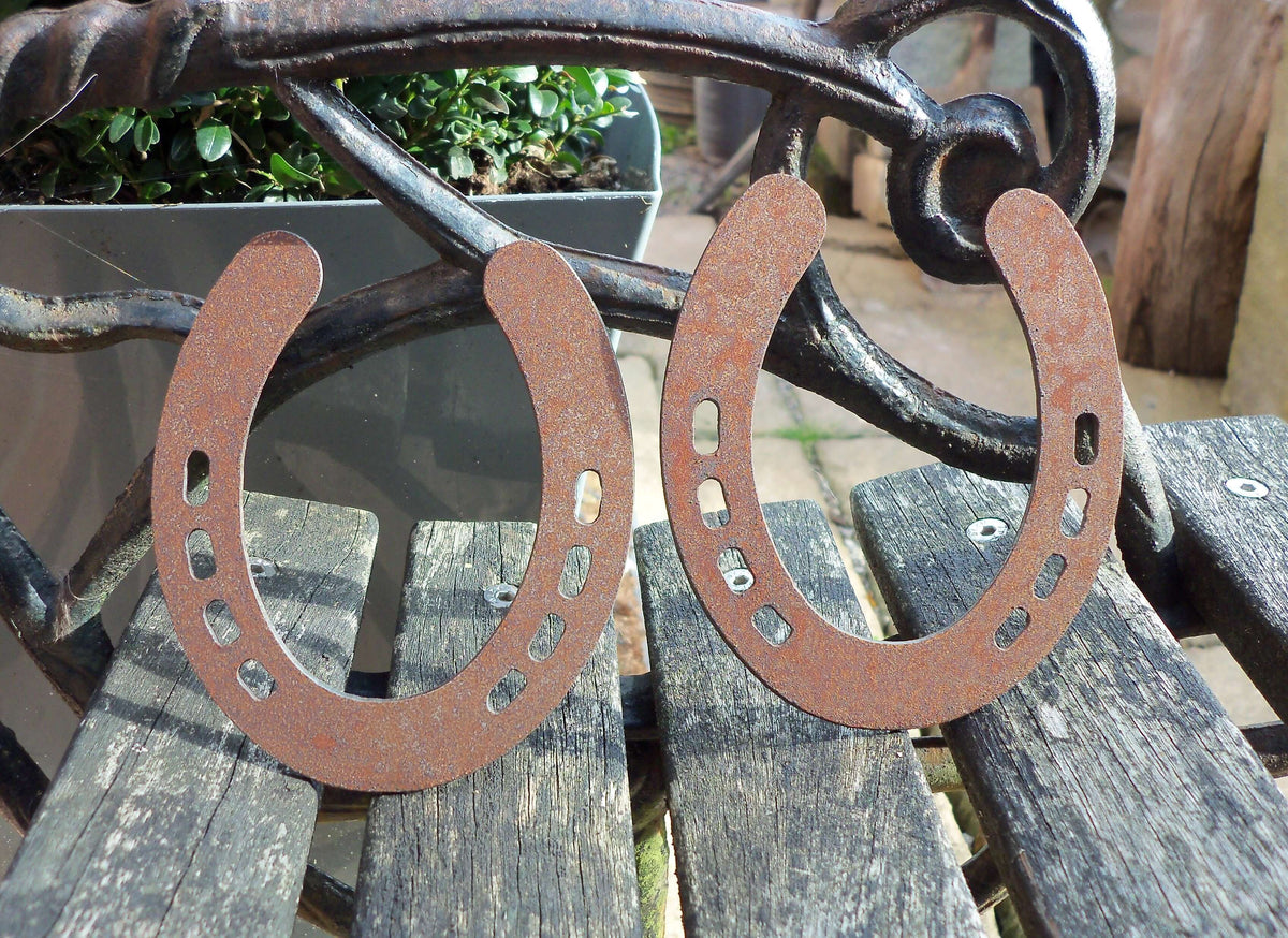 Rusty Steel PAIR OF HORSESHOES Garden Ornaments displayed on a wooden bench, showcasing their unique rustic metal design.