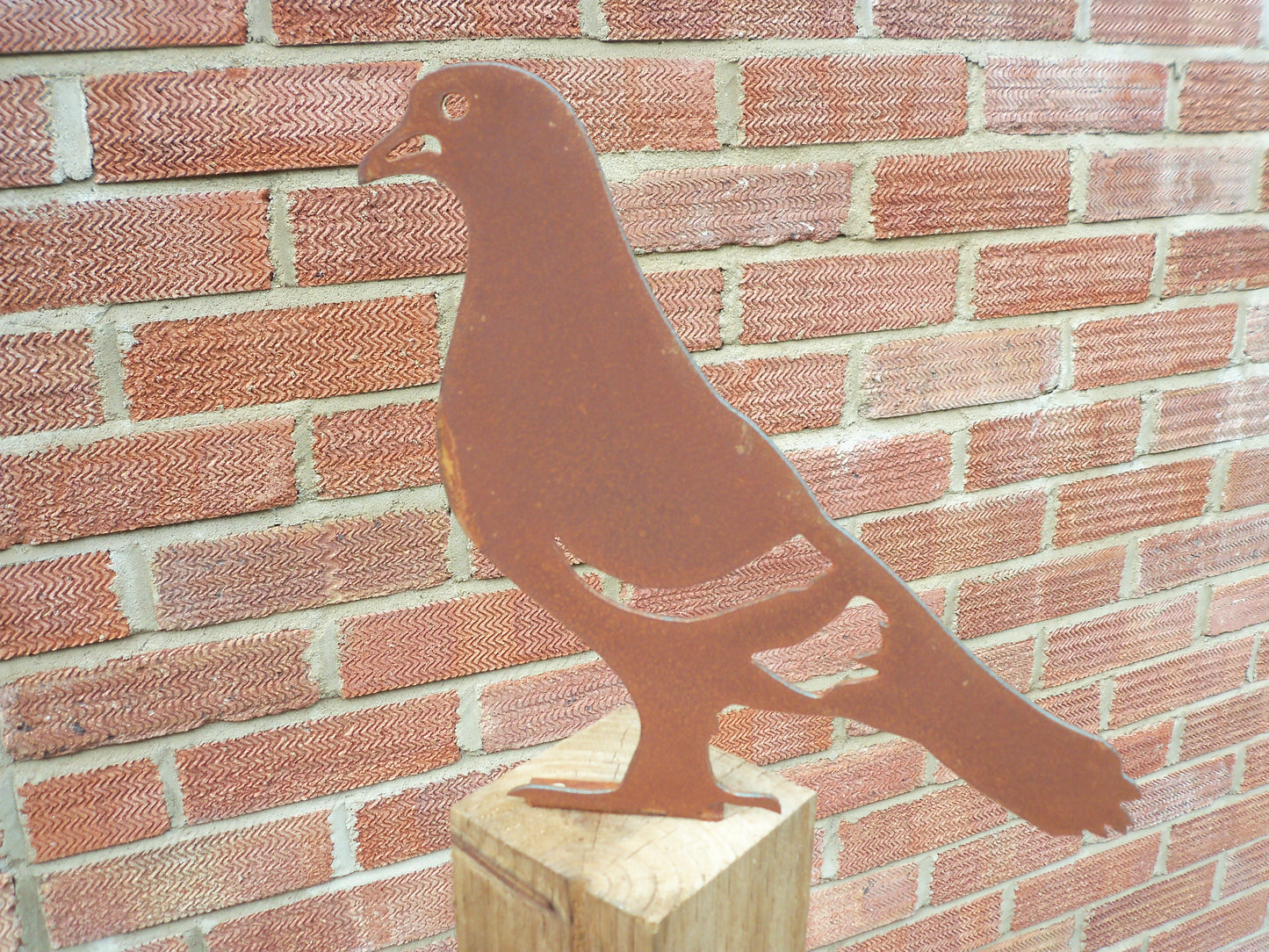 Rusted metal pigeon post topper against a red brick wall, great industrial style garden art.