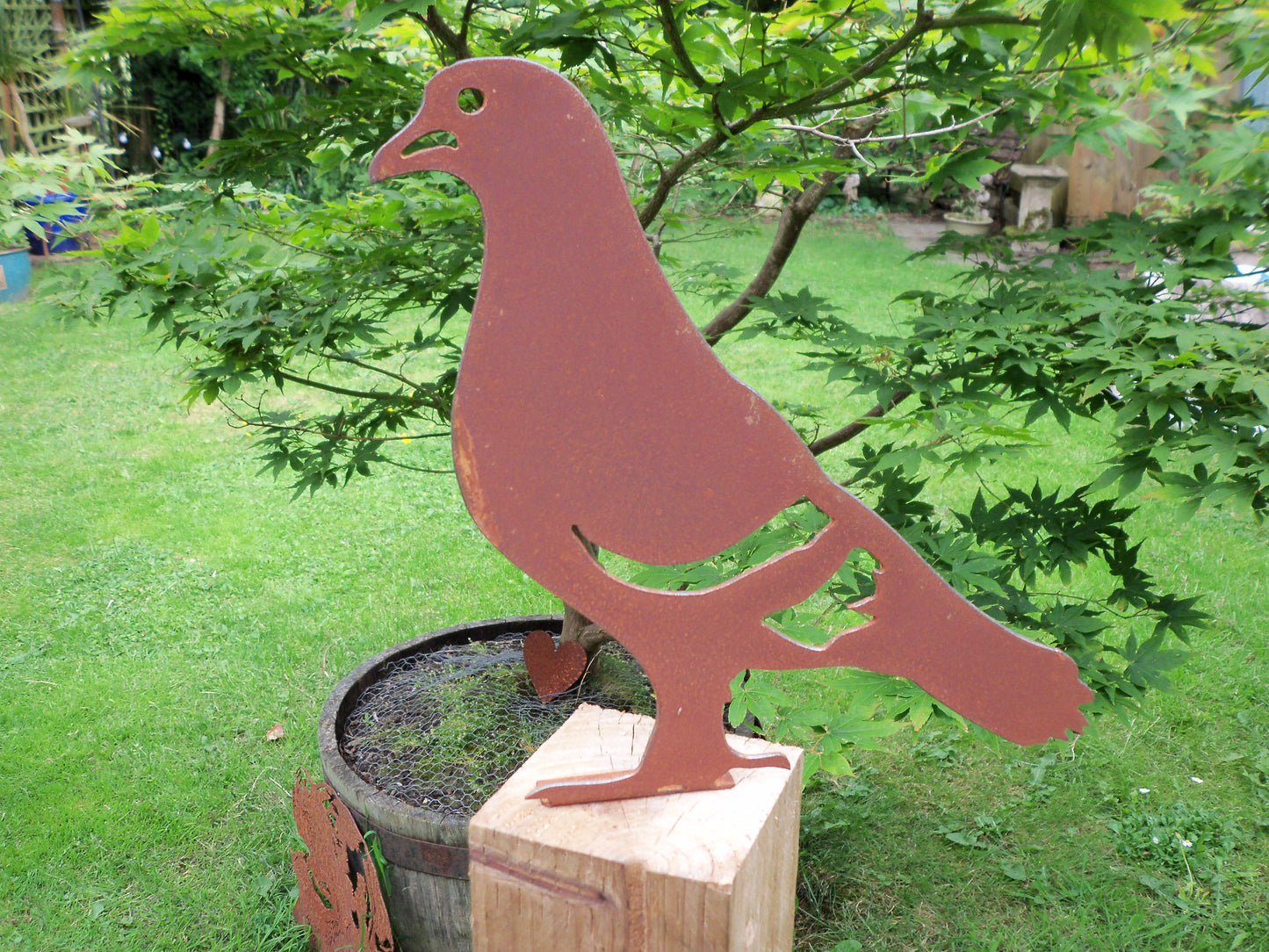 Rustic metal pigeon post topper in front of a maple tree, perfect garden decor, unique rusted patina effect.