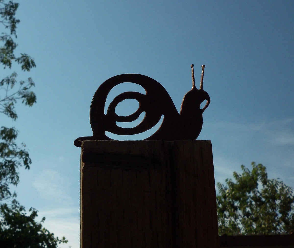 Rusty Steel Snail Garden Ornament perched on a fence post against a clear sky.