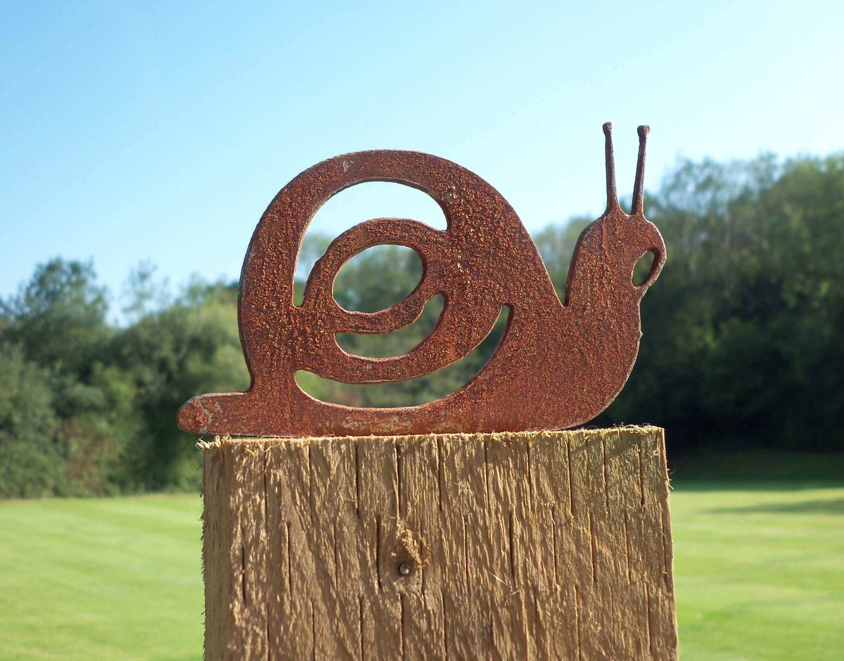 Rusty Steel Snail Garden Ornament on wooden post with green garden background, unique rustic metal decoration.