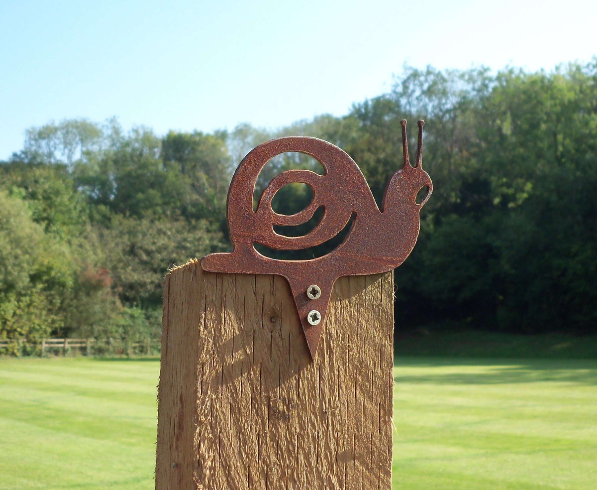 Rusty Steel Snail Garden Ornament on a fence post, showcasing rustic metal decoration in a garden setting.