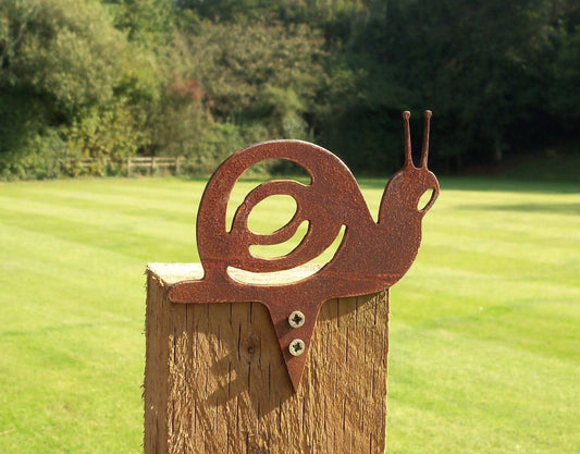 Rustic metal snail garden ornament fixed to a post in a green field, rusted steel garden art.