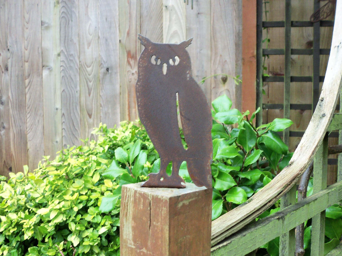Rusted Steel Owl Garden Ornament perched on a wooden fence post amidst greenery, adding rustic charm to the garden.