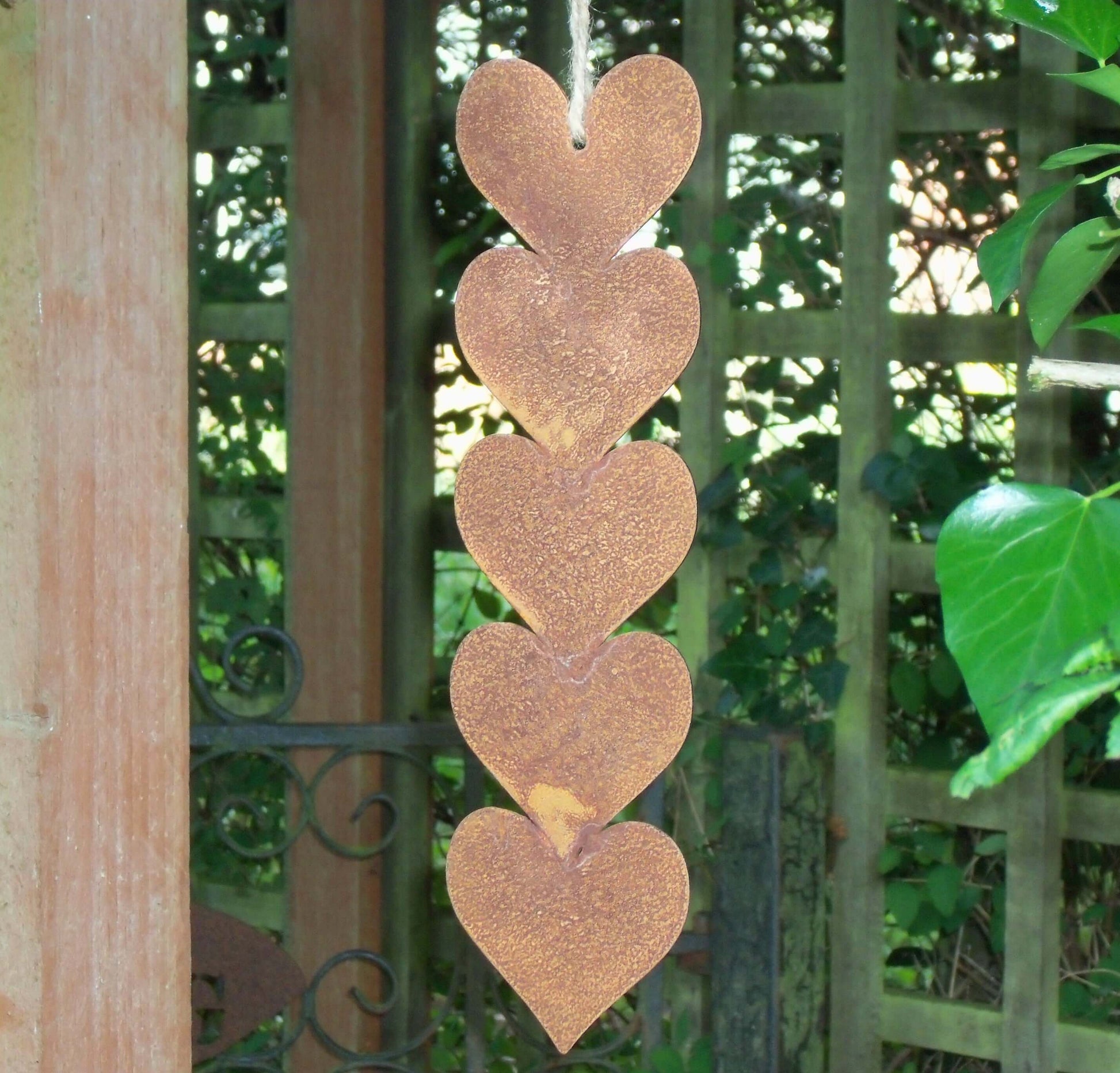 Rusty metal hanging hearts garden ornament showcased in a garden setting, with five hearts on a jute string.