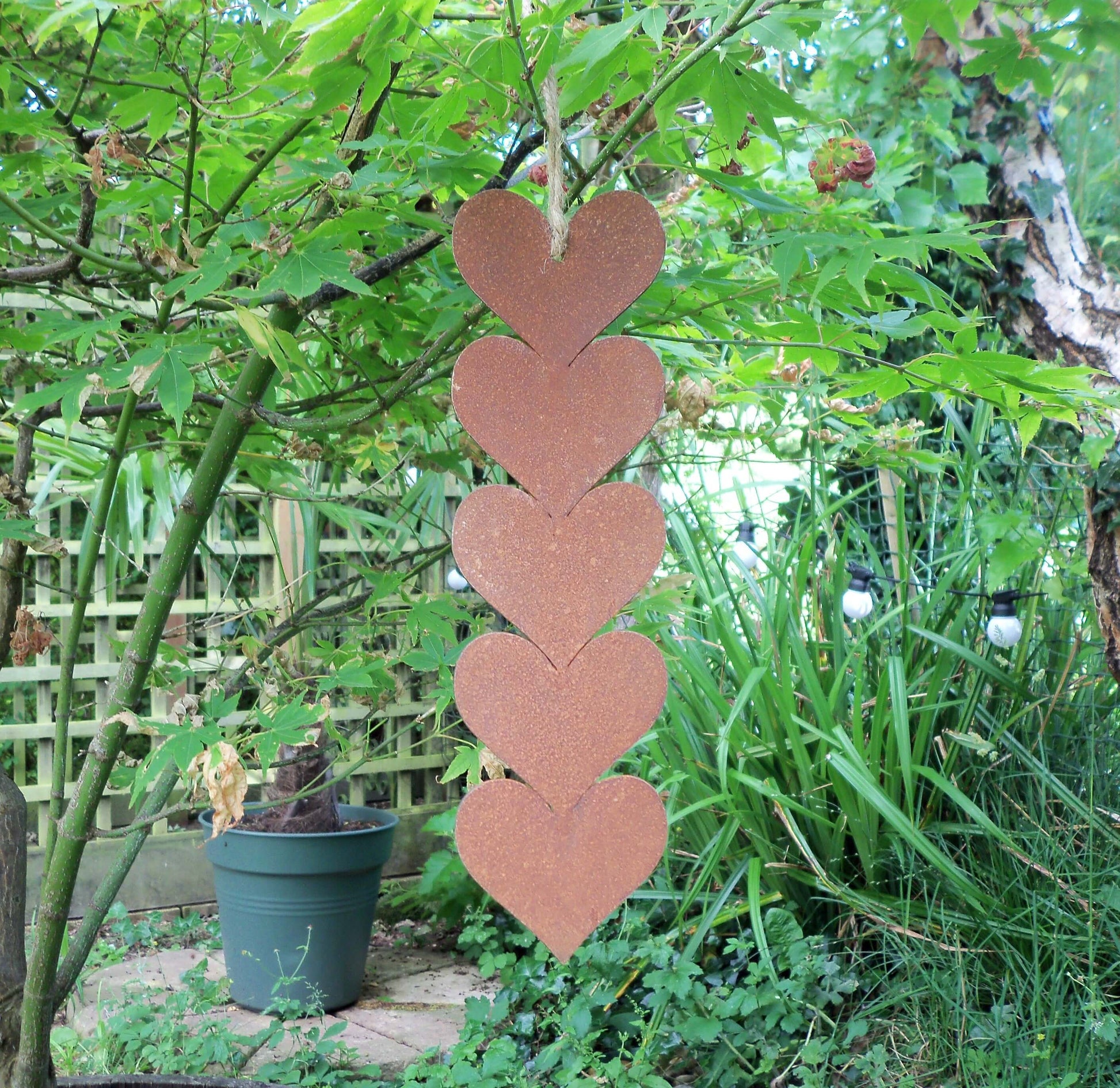 Rusty metal hanging hearts garden ornament displayed among greenery in a garden setting.