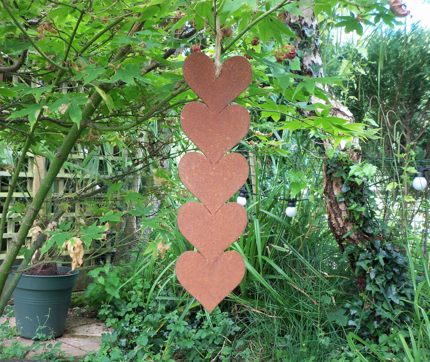 Rusty metal hanging hearts garden ornament displayed outdoors among green foliage.