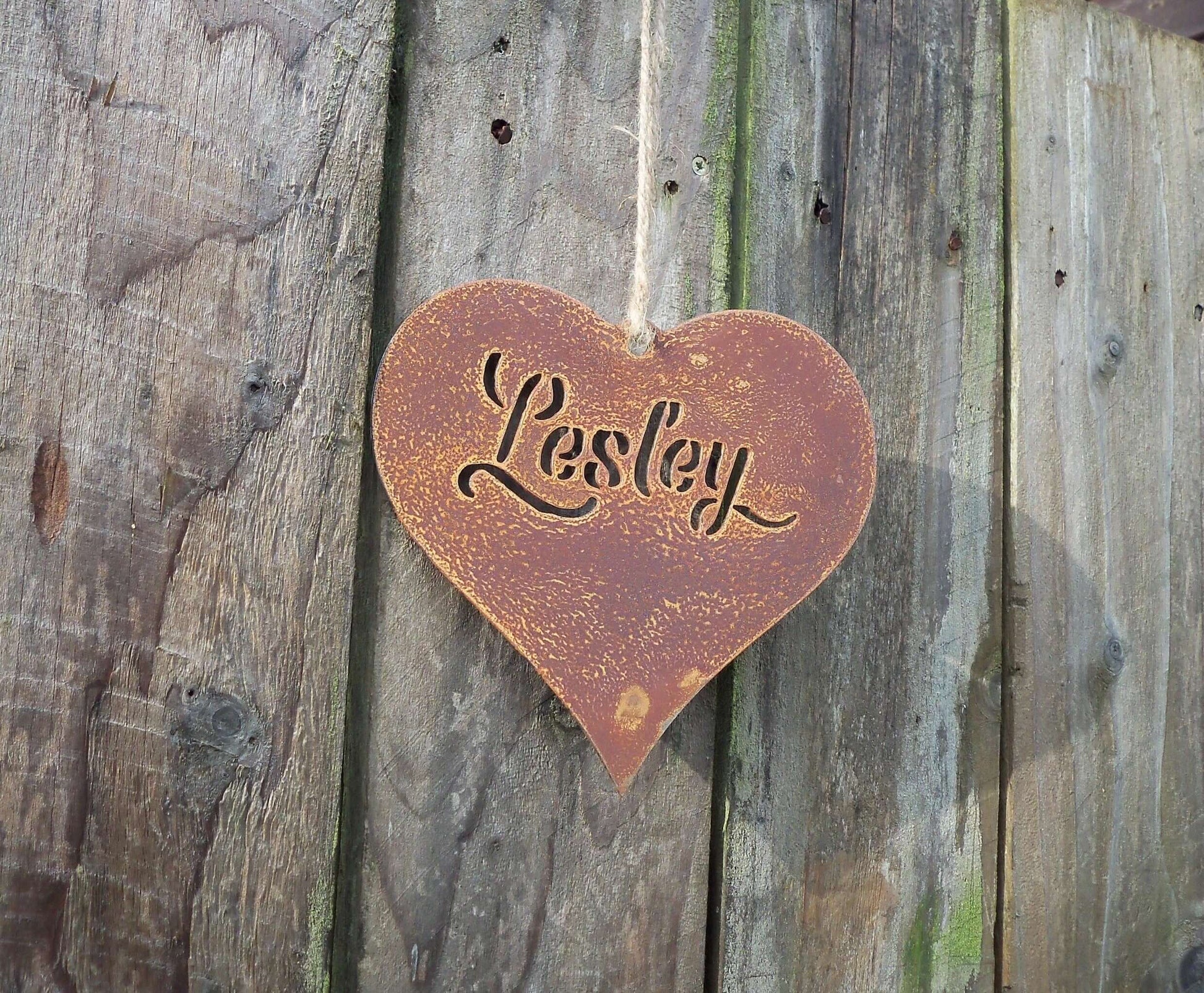 Weathered Personalised rusty metal hanging heart ornament hanging on a fence