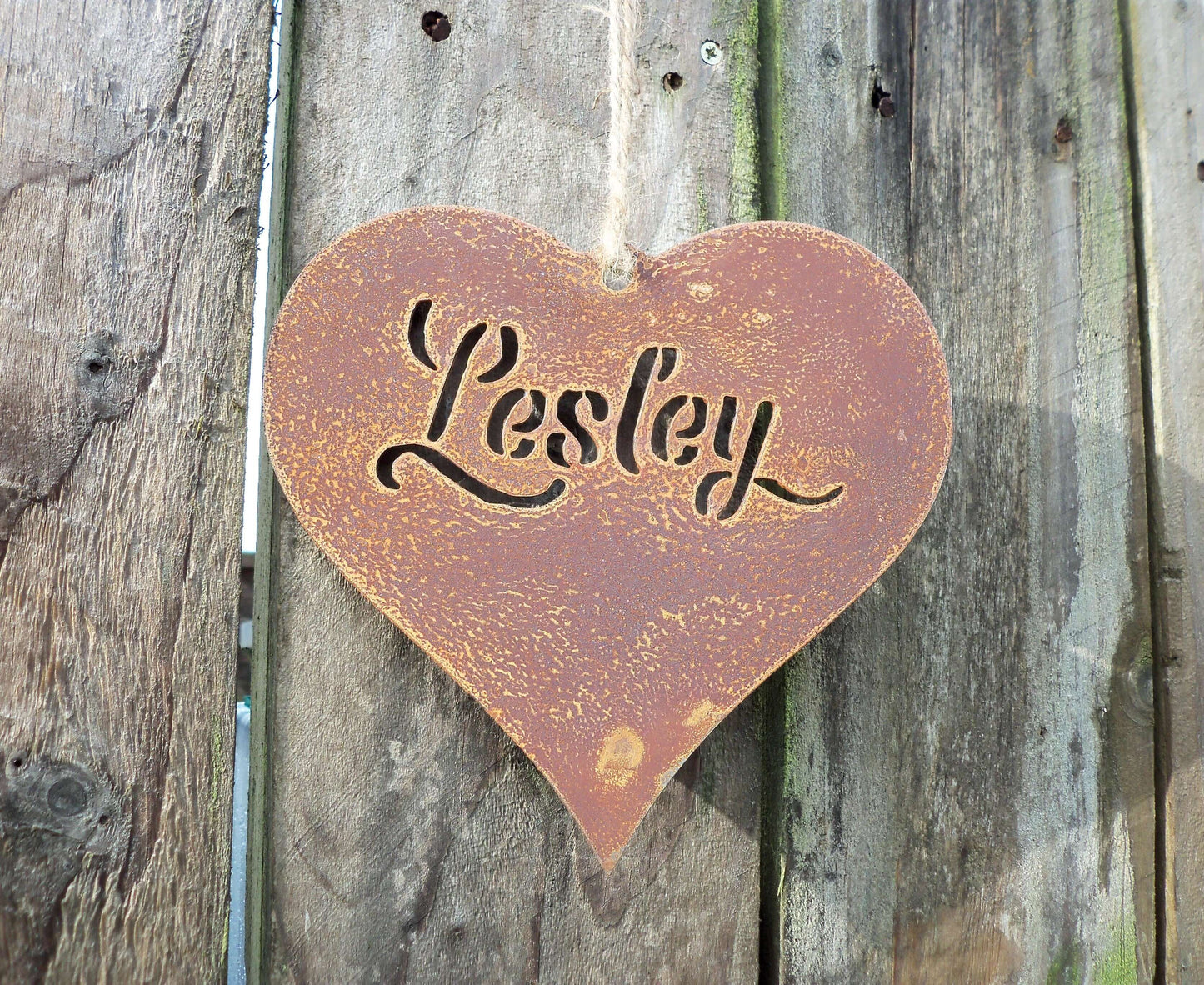 Personalised rusty metal hanging heart ornament hanging beside a fence