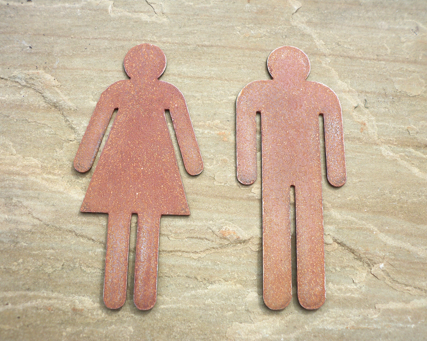 Rustic Metal WC Toilet Door Signs of a male and female figure on a stone surface