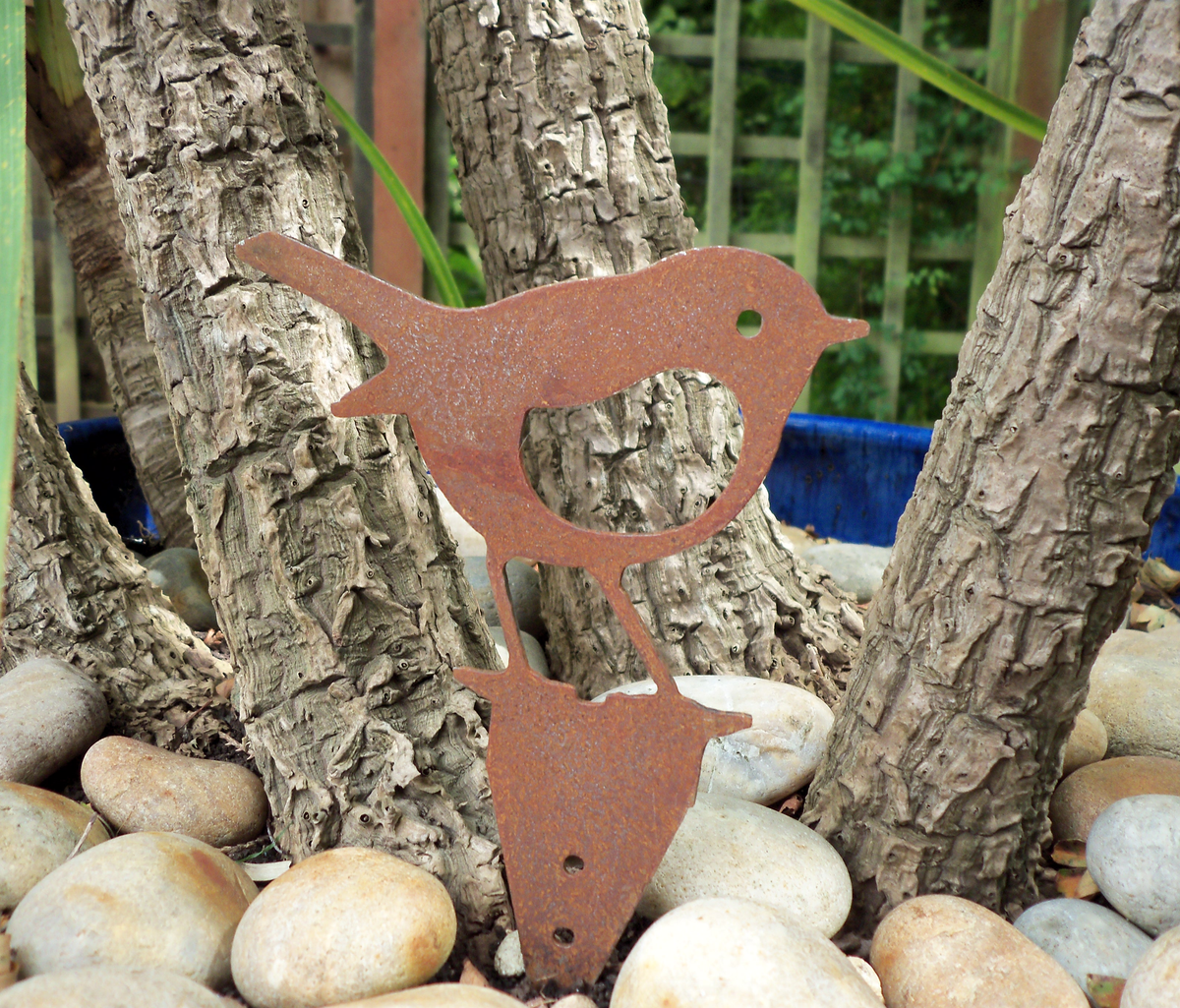 Rusty Steel Robin Garden Ornament among pebbles and trees, showcasing rustic metal garden art for outdoor decor.