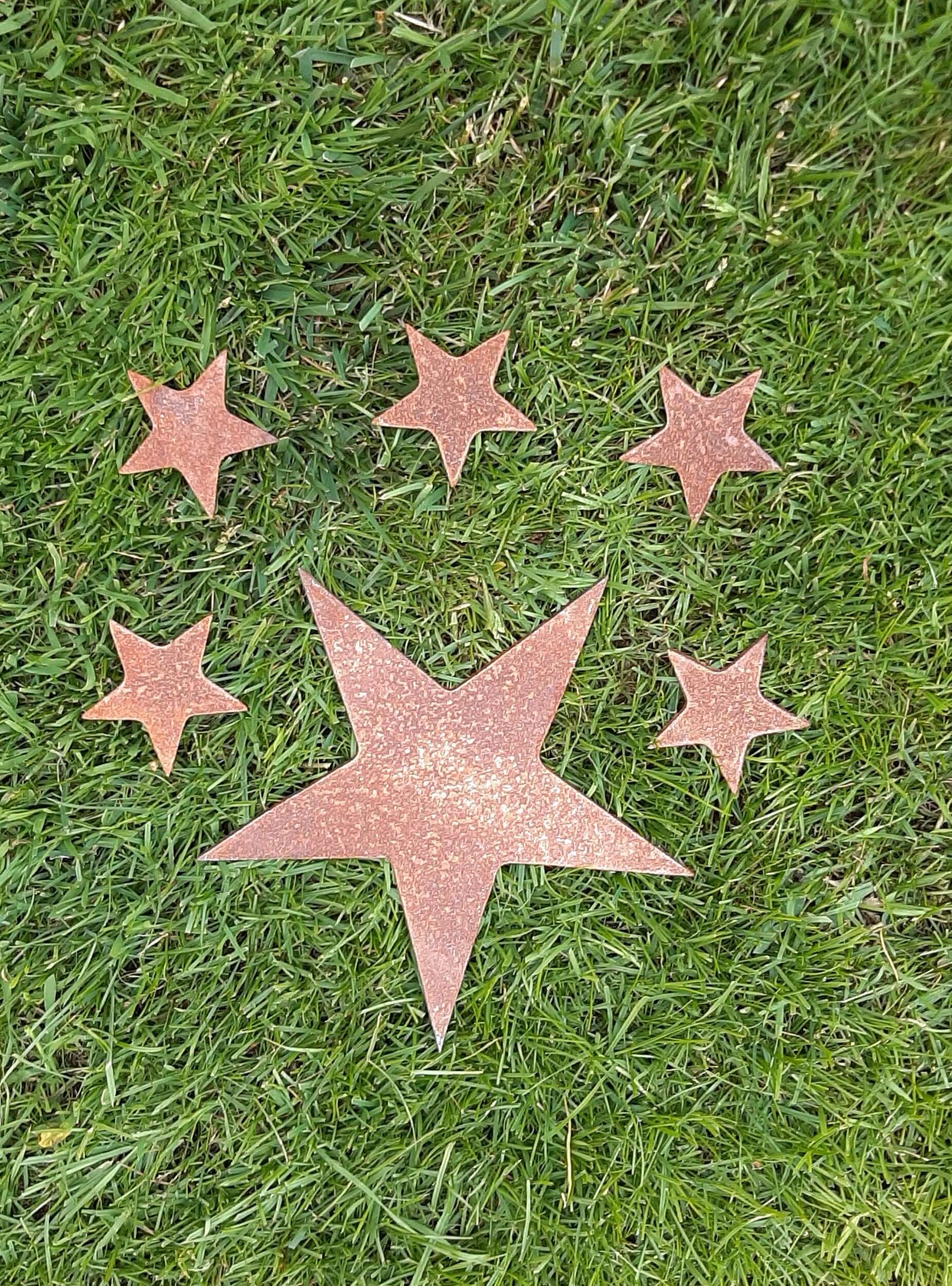 Five-pointed rusty metal star surrounded by four smaller stars in a grassy field