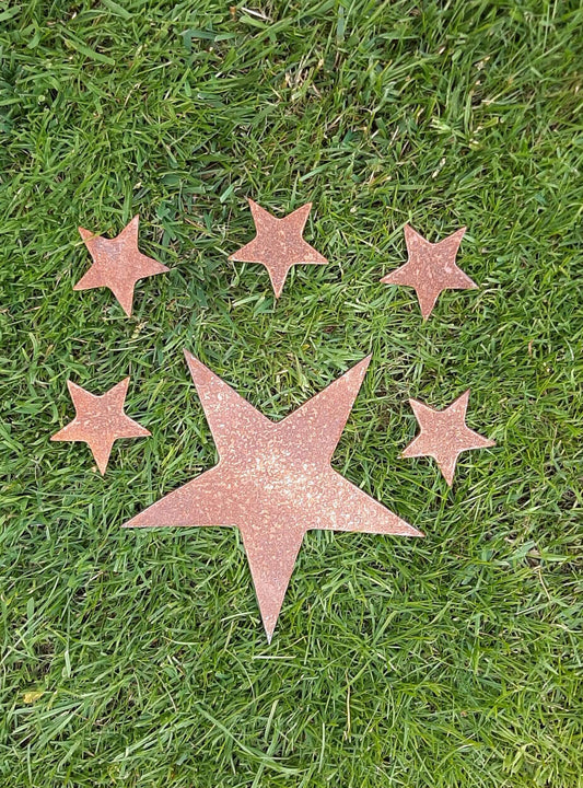 Five-pointed rusty metal star surrounded by four smaller stars in a grassy field