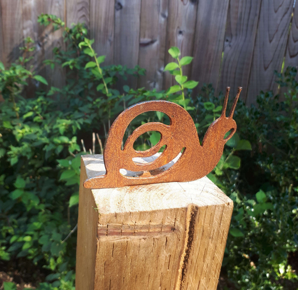 Rusty Steel Snail Garden Ornament perched on a wooden fence post in a garden setting.