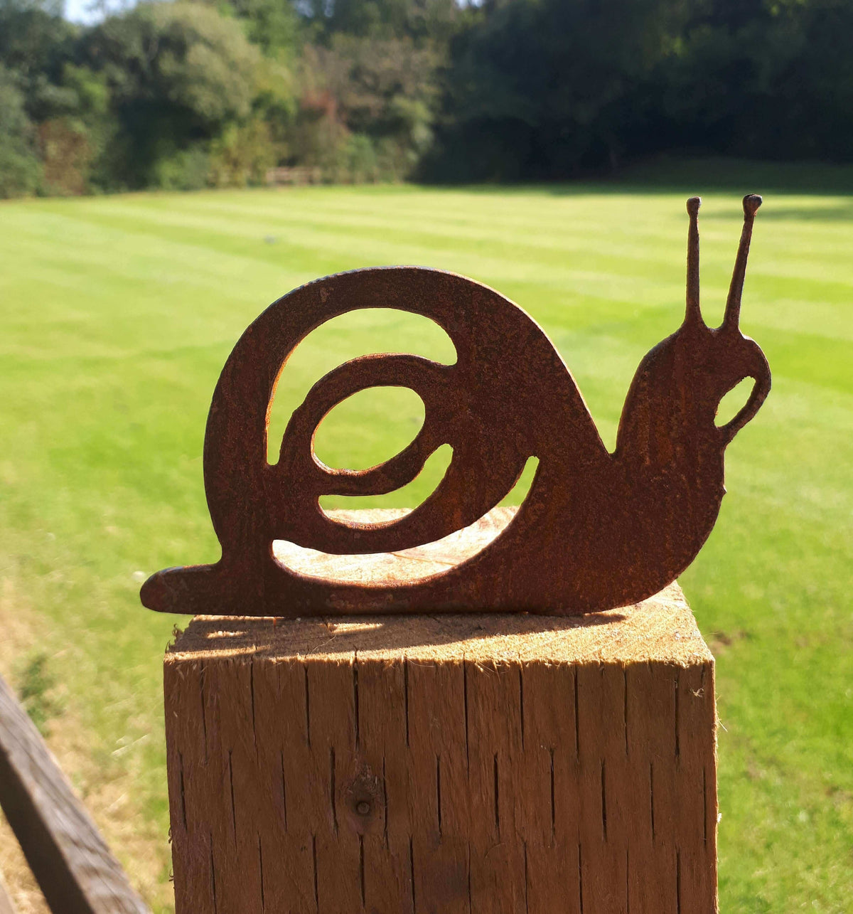 Rusty Steel Snail Garden Ornament perched on a wooden post in a green garden setting.