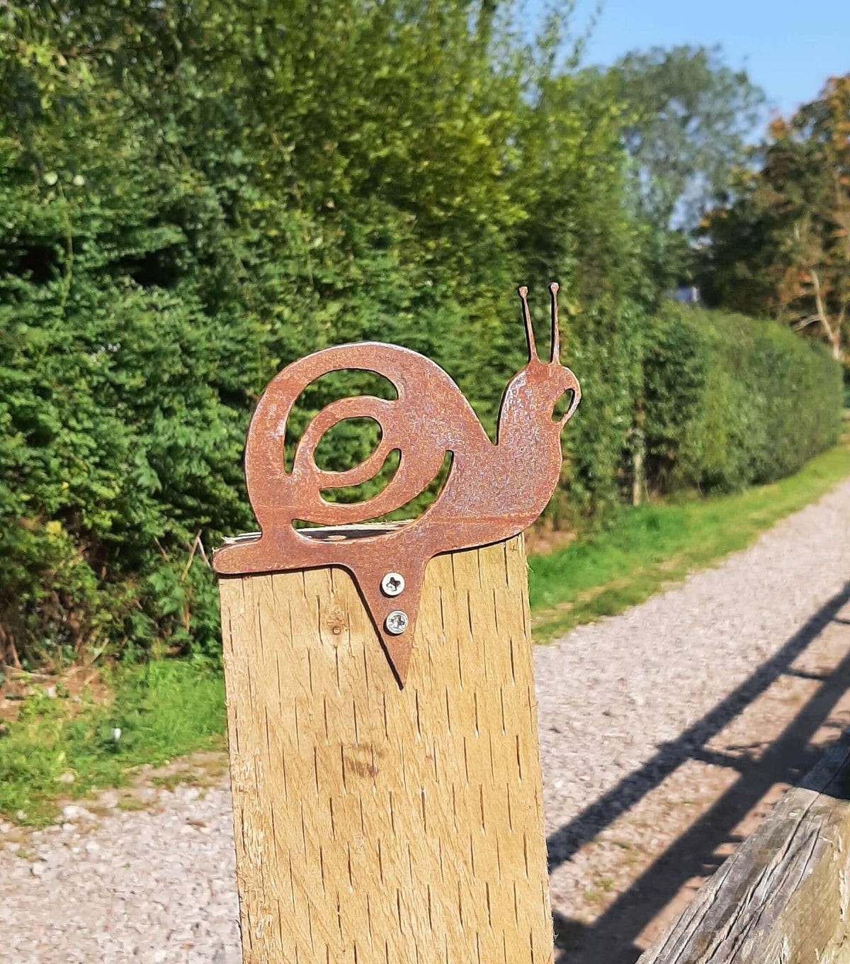 Rusty Steel Snail Garden Ornament mounted on a fence post, adding rustic charm to outdoor spaces.