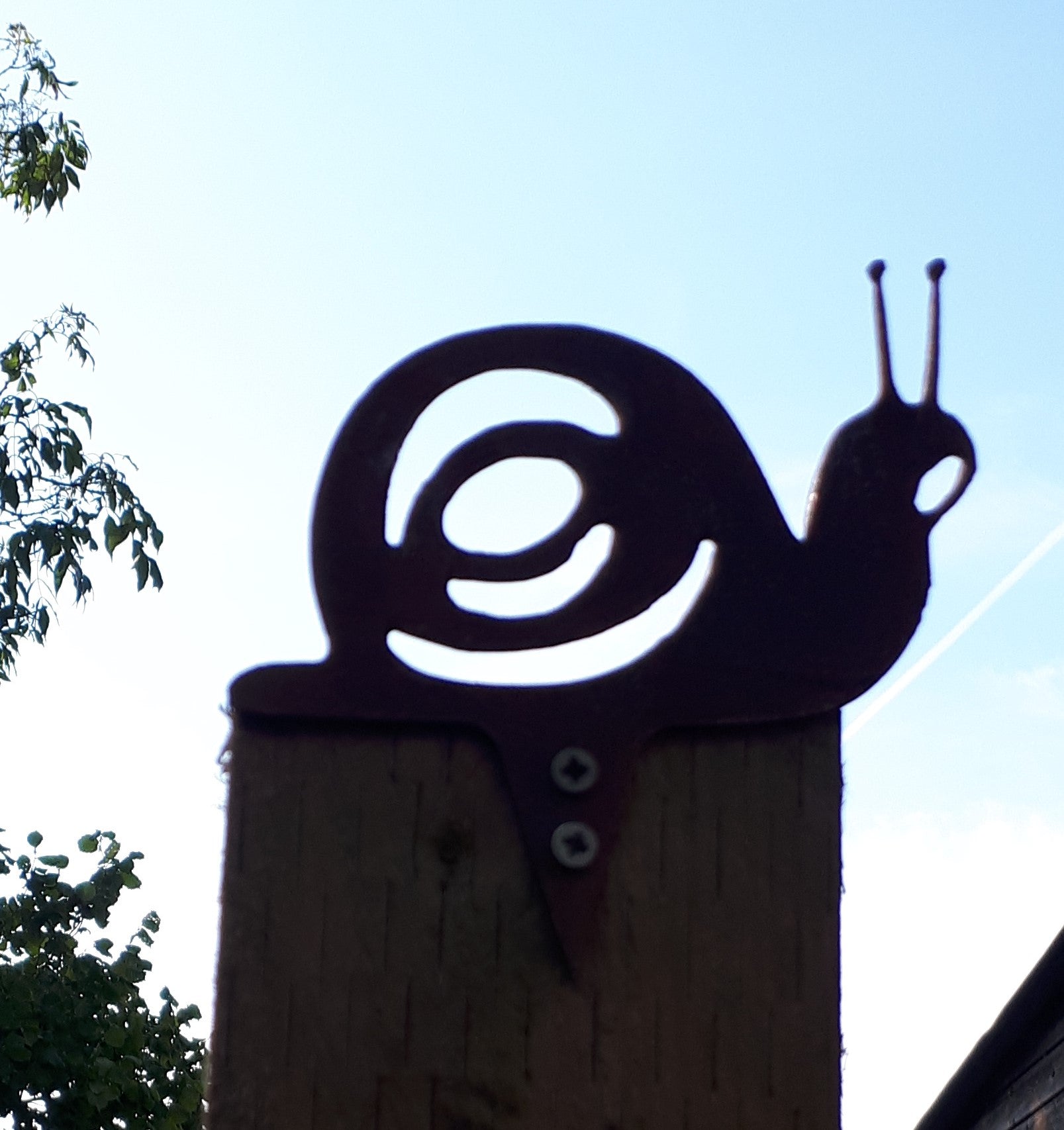 Rusty metal snail garden decoration fixed to a post against an early autumn sky, perfect garden art gift.