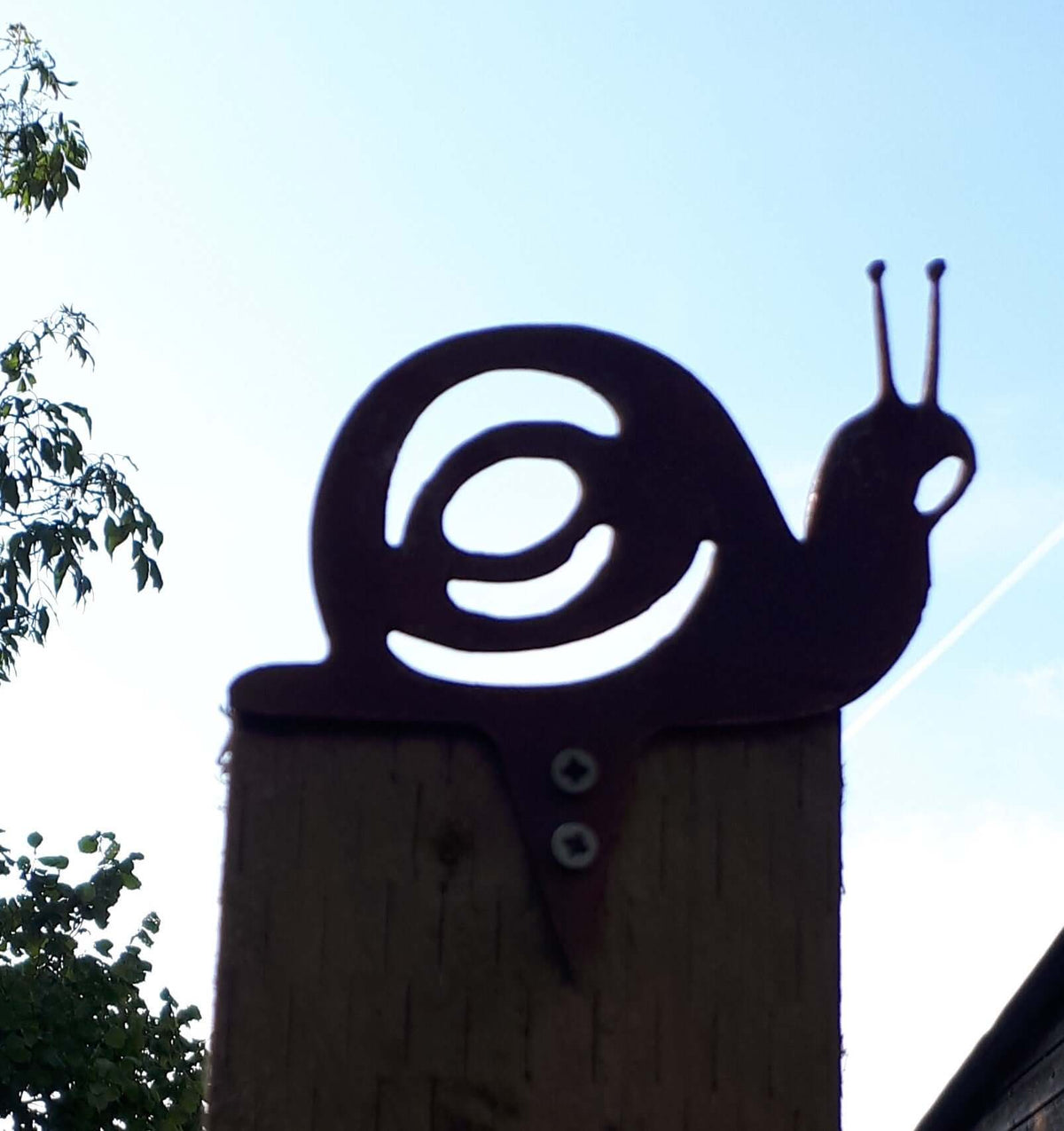 Rusty Steel Snail Garden Ornament perched on a fence post, adding rustic charm to outdoor decor.