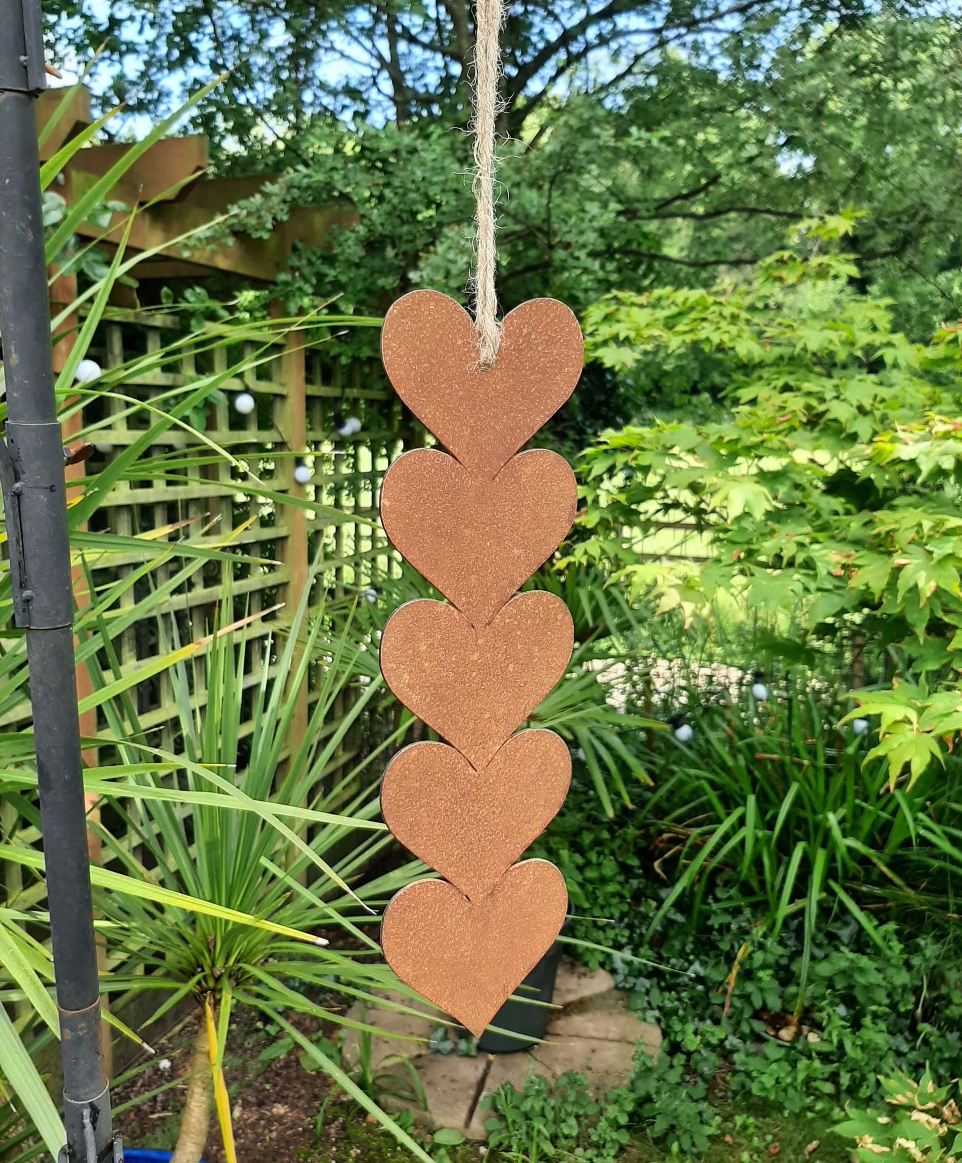 Rusty metal hanging hearts garden ornament displayed in a garden setting with greenery.