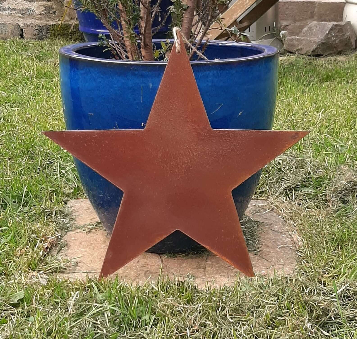 Rusty Metal STAR Garden Ornament on a stone base with a blue pot and plant in the background.