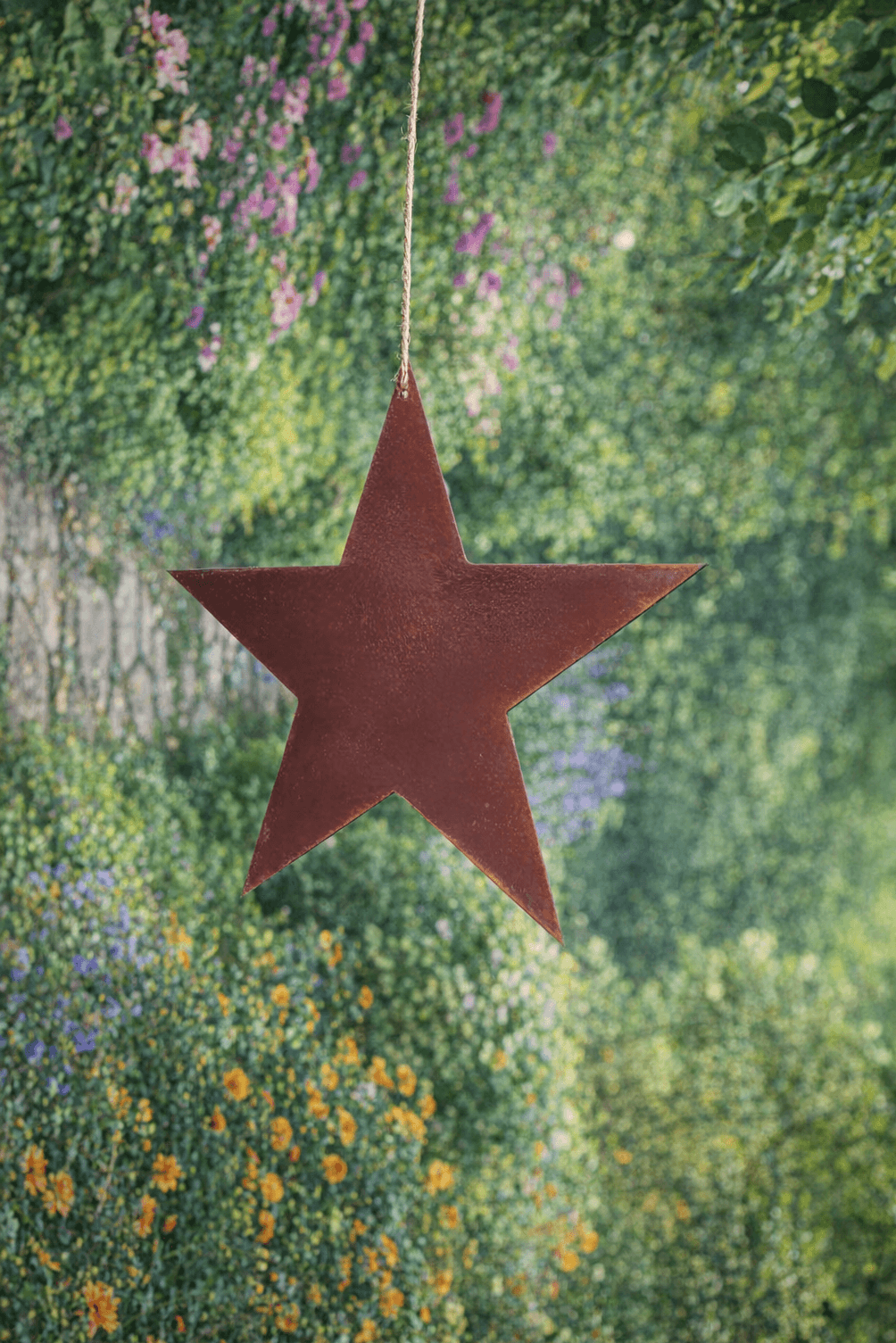 Rusty Metal STAR Garden Ornament decoration hanging in a garden with flowers and greenery.