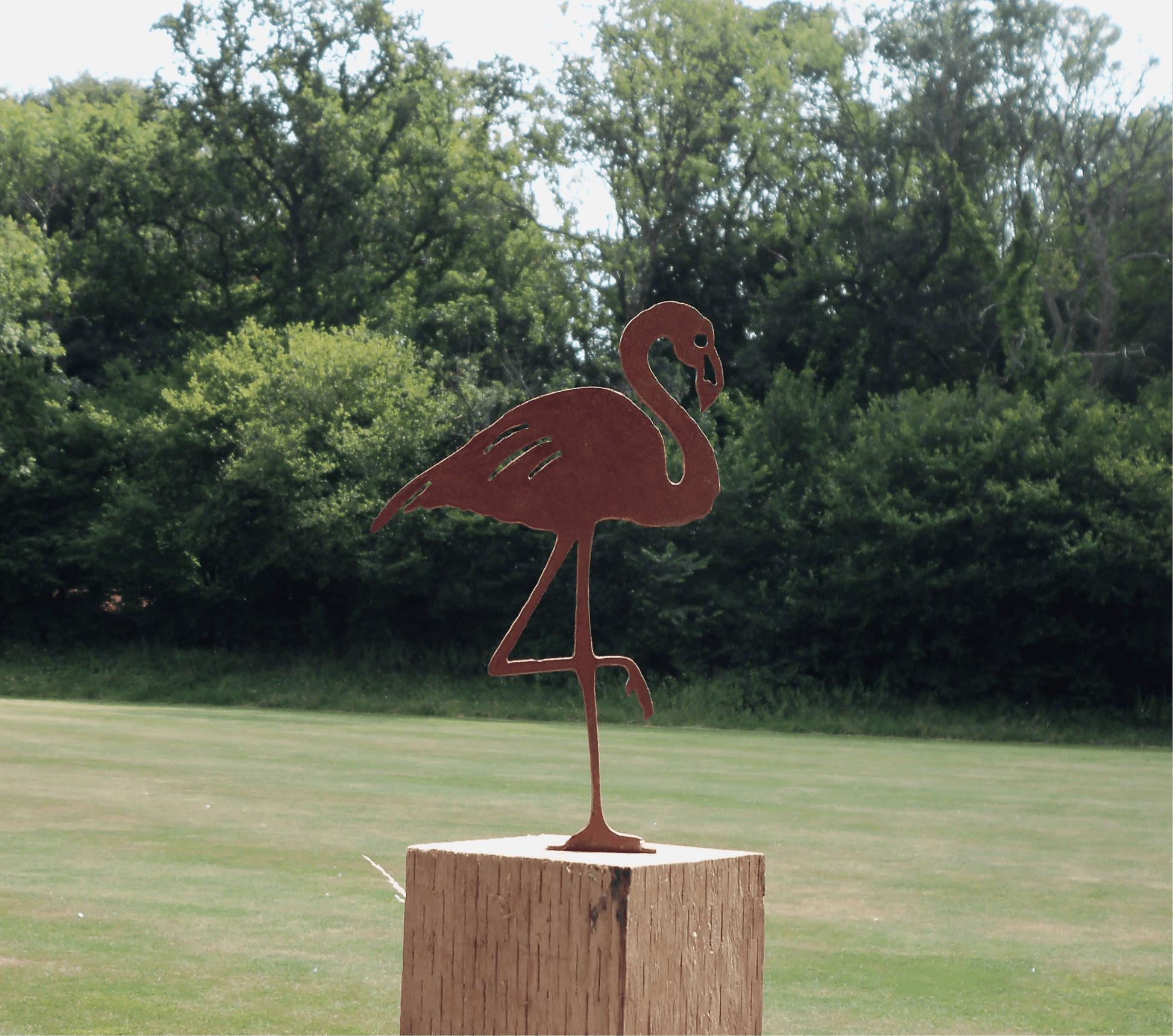 Rusty Metal Flamingo garden ornament on wooden post in garden, showcasing rustic decor with industrial style.