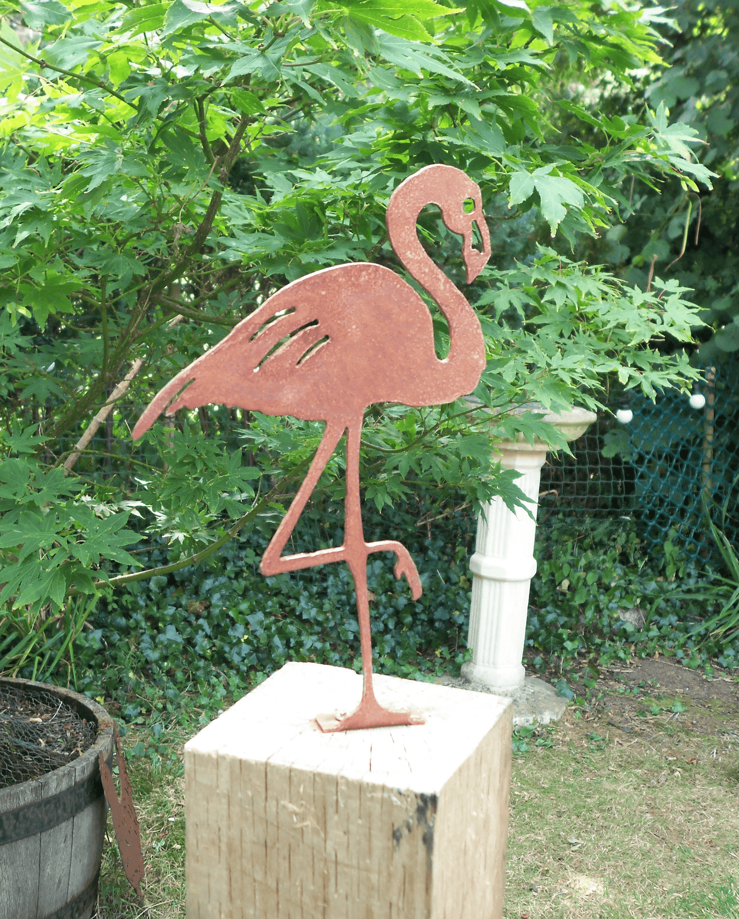 Rusty Metal Flamingo garden ornament displayed in a garden setting with greenery in the background.