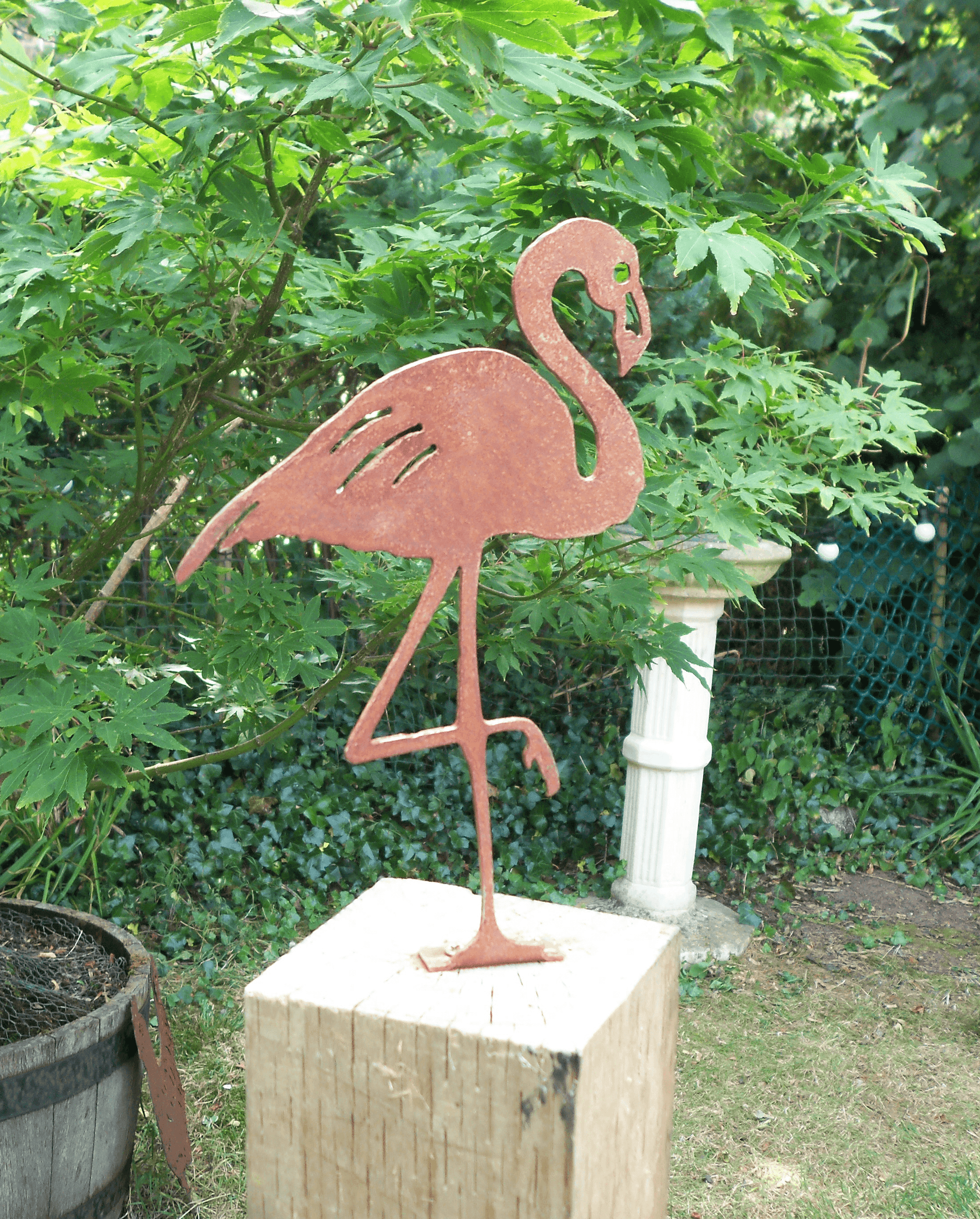 Rusty Metal Flamingo garden ornament displayed in a garden setting with greenery in the background.