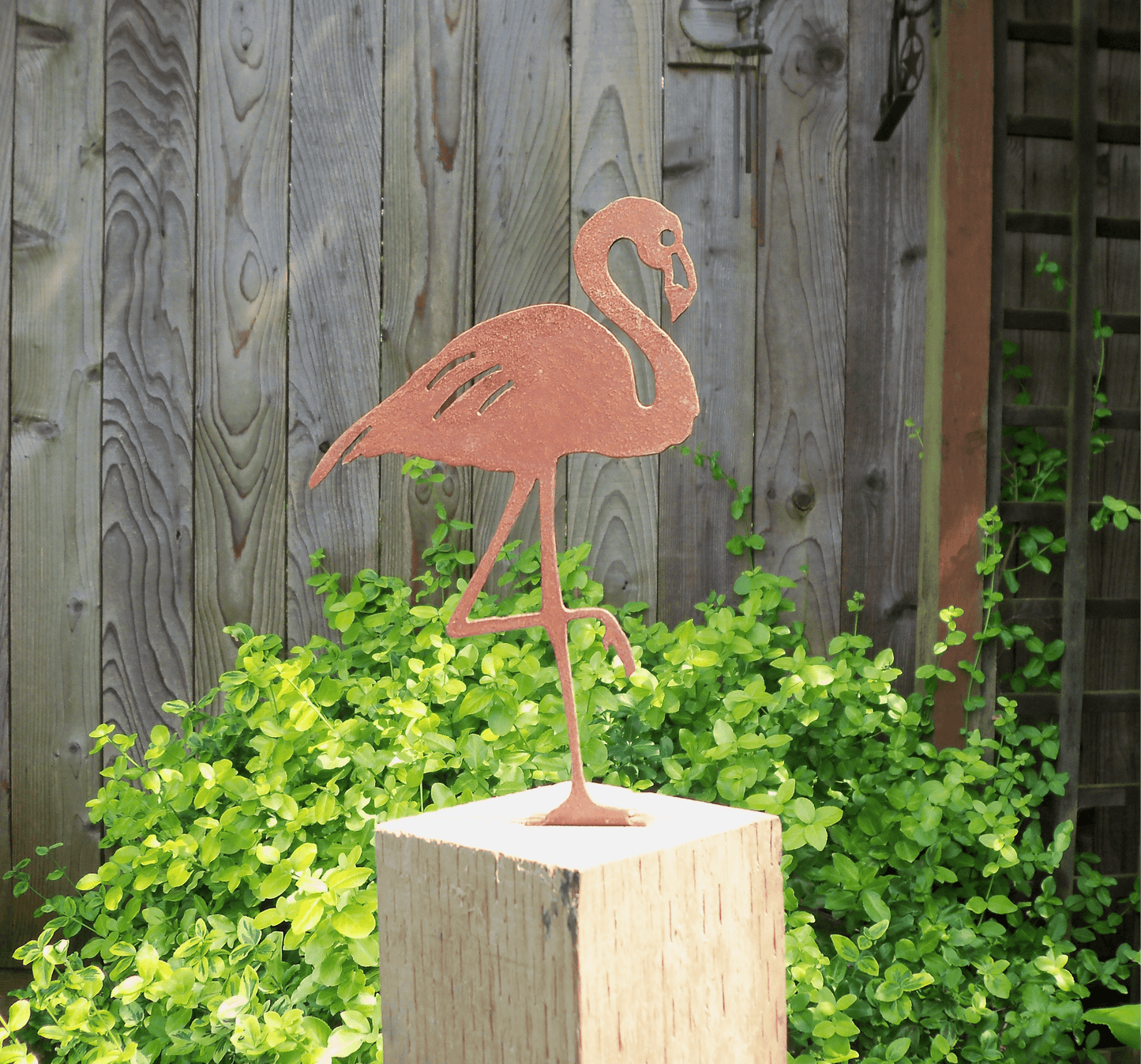 Rusty Metal Flamingo garden ornament on a wooden post with greenery in the background.
