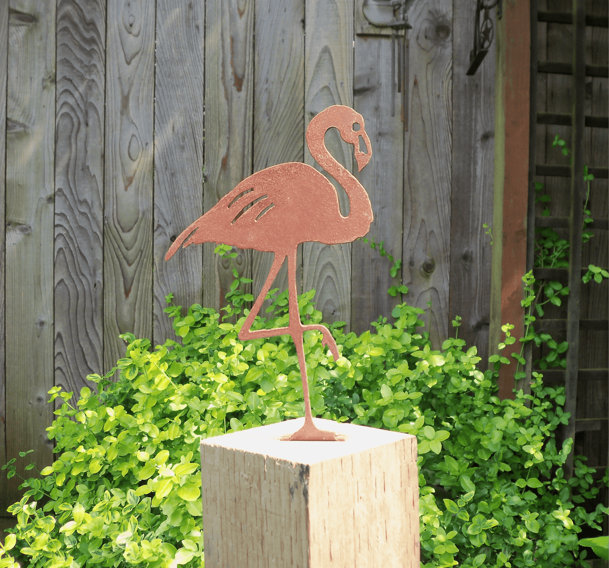 Rusty Metal Flamingo garden ornament on a wooden post with greenery in the background.