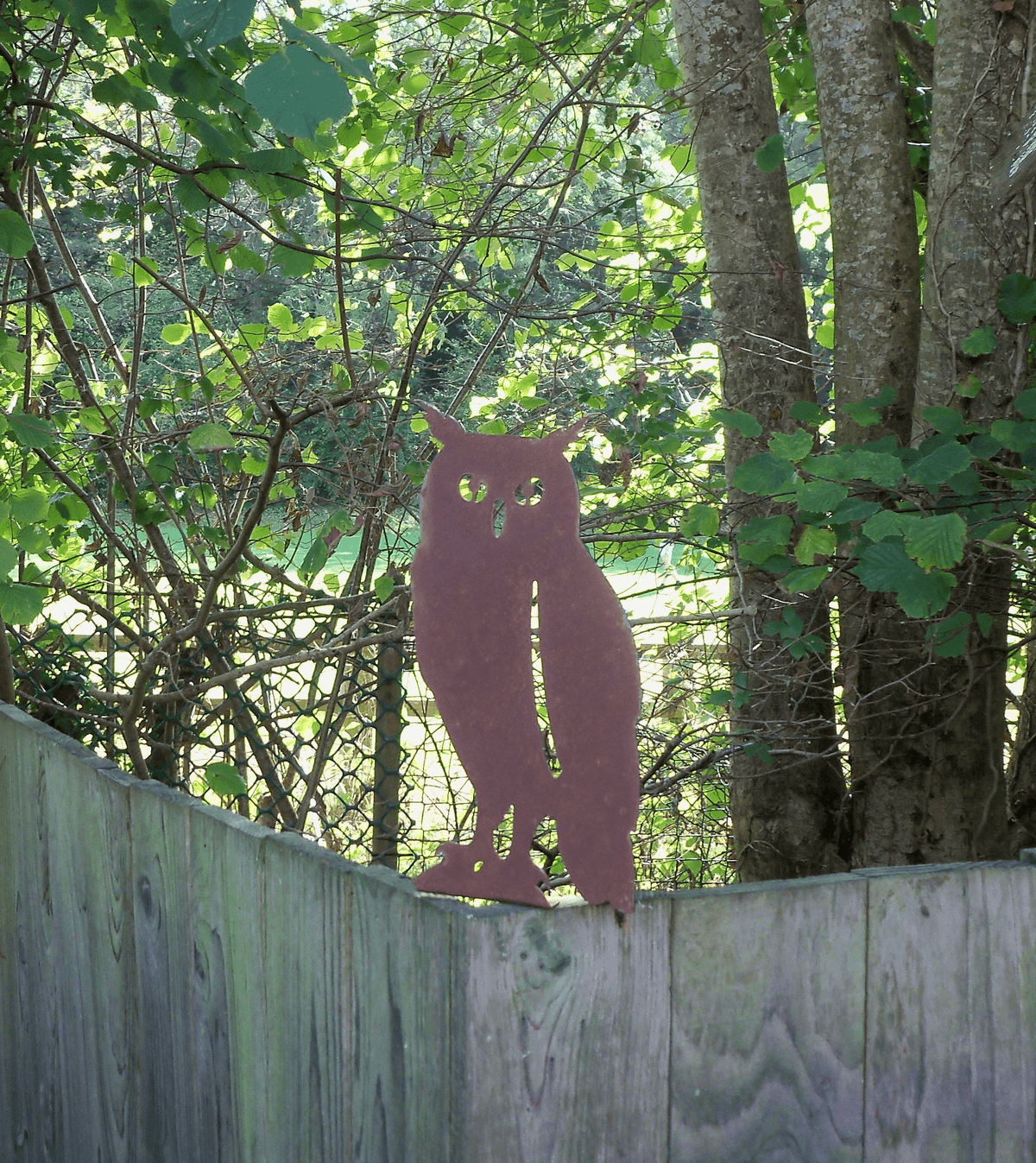 Rustic Steel OWL Garden Ornament displayed atop a wooden fence in a lush garden setting.