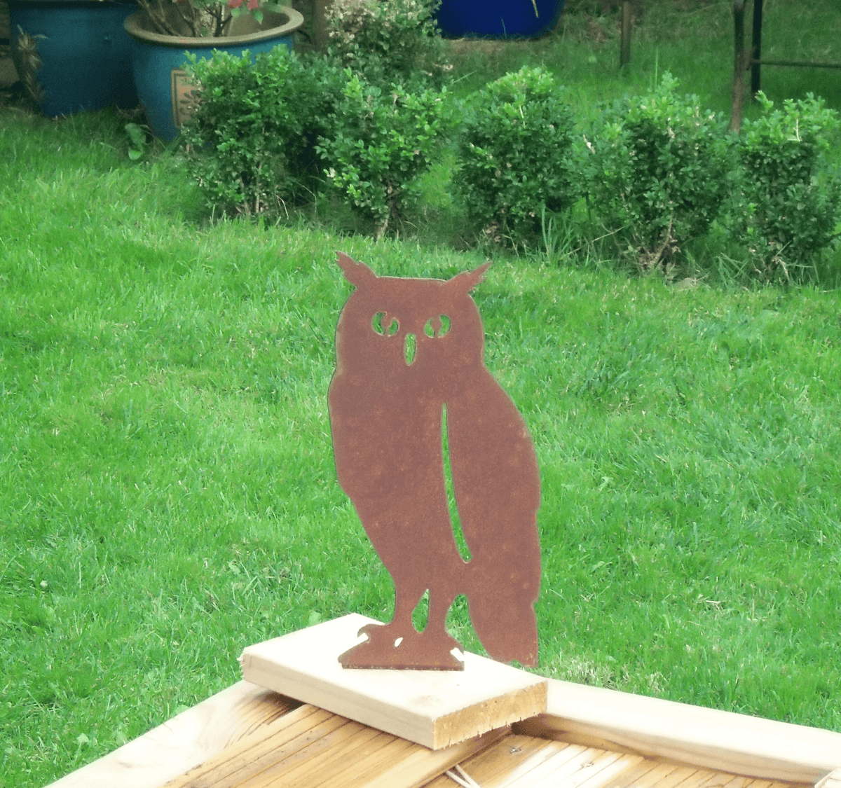 Rustic Steel OWL Garden Ornament standing on a wooden base in a green garden, showcasing its rustic charm and unique patina finish.