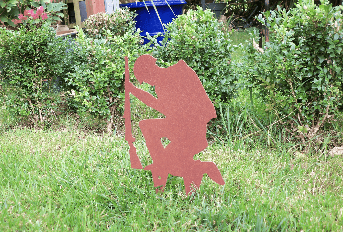 Rustic Steel SOLDIER Garden Ornament showing a kneeling soldier with a rifle in a garden setting.