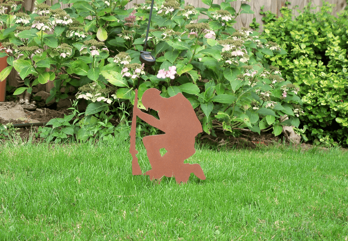 Rustic Steel SOLDIER Garden Ornament displayed in a garden setting among flowers and grass.