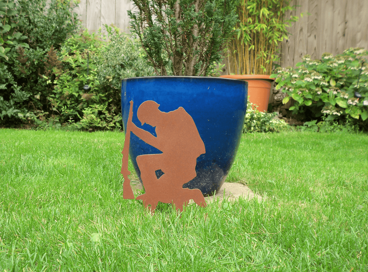 Rustic Steel SOLDIER Garden Ornament displayed in garden with blue pot, featuring a kneeling soldier silhouette.